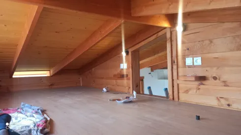Habitación tipo loft revestida de madera, con techo inclinado, tragaluces y algunos objetos en el suelo