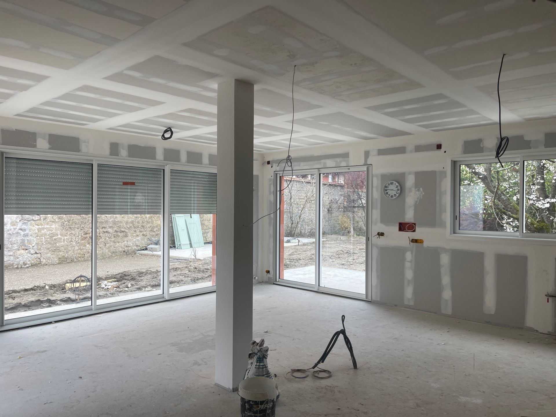 Travail de plaquisterie en cours de ponçage dans un salon avec baies coulissantes