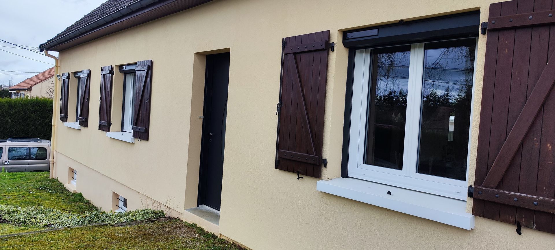 Façade de maison avec des fermetures blanches et des volets en bois marron foncé