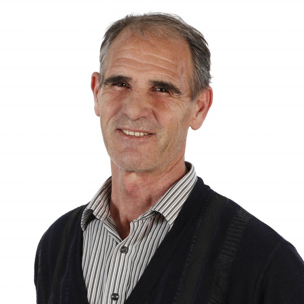 Ein Mann in schwarzem Pullover und gestreiftem Hemd lächelt in die Kamera