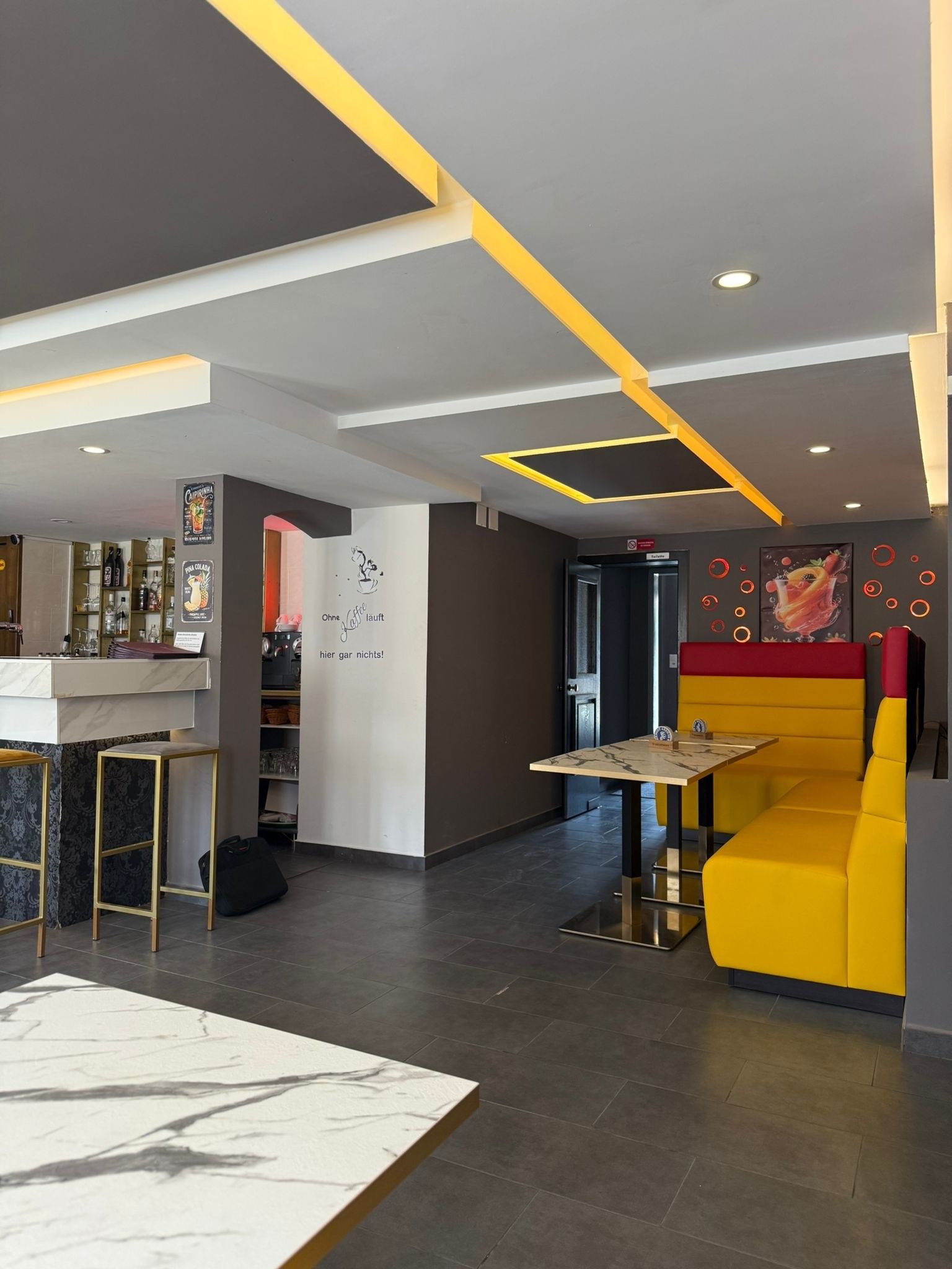 Moderne Lounge mit gelben Sitznischen, Stehtischen, Barhockern und geometrischen Deckenleuchten
