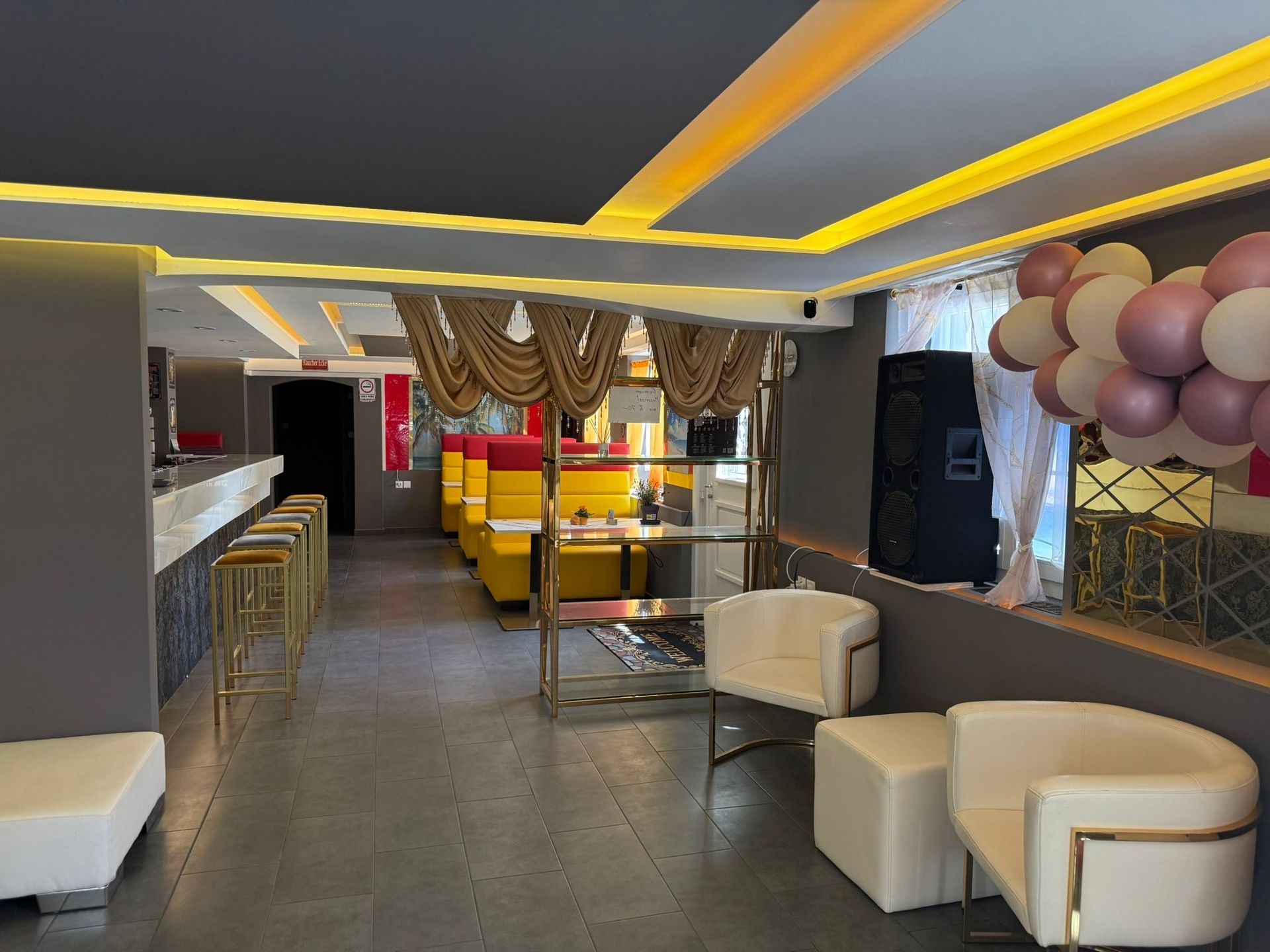 Moderne Lounge mit gelben Deckenleuchten, weissen Sitzmöbeln, Barhockern und einer mit Luftballons dekorierten Wand