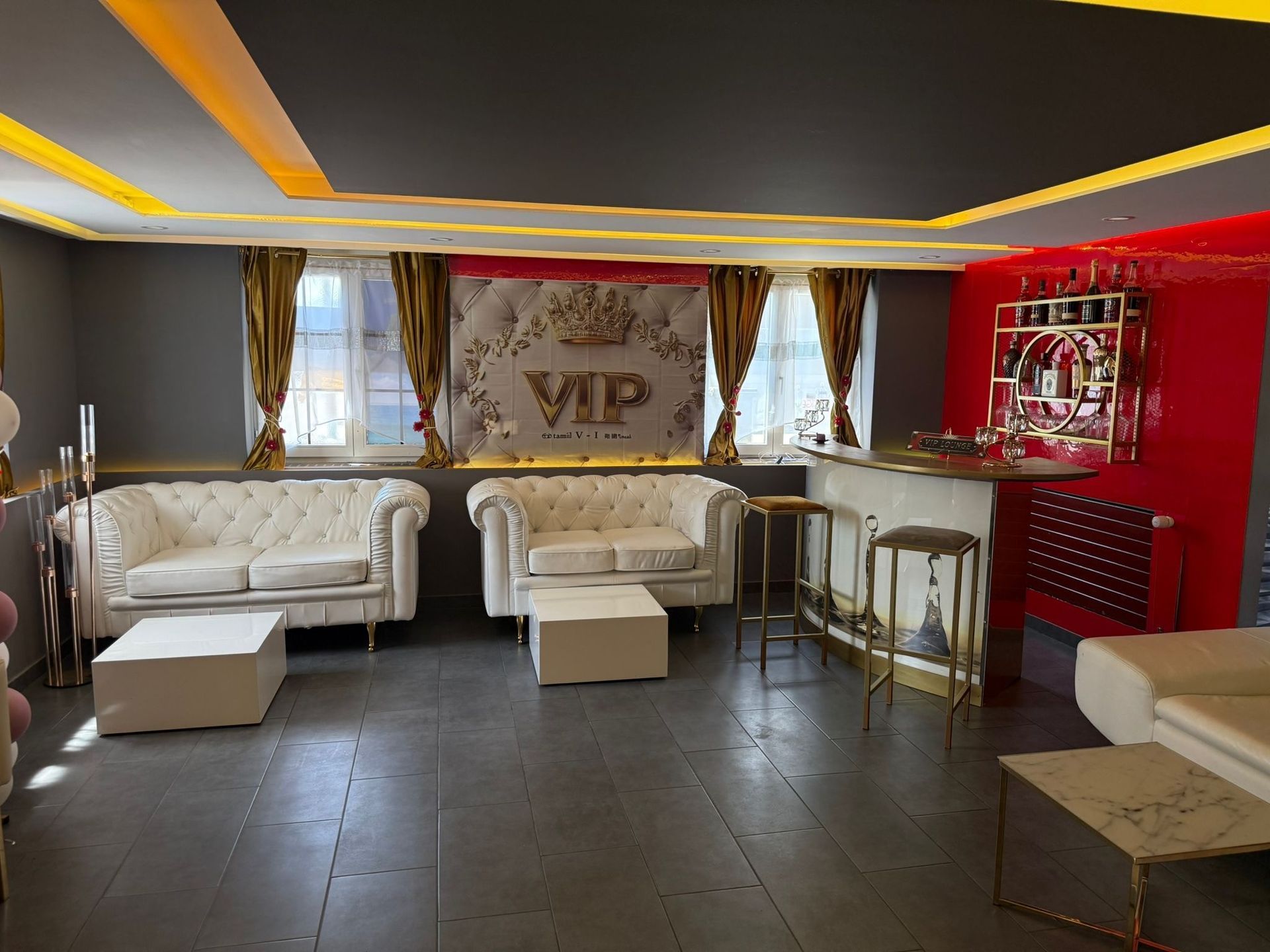 Moderne Lounge mit weissen Sofas, goldener Dekoration, dunklem Fliesenboden und roter Akzentwand mit Neonreklame