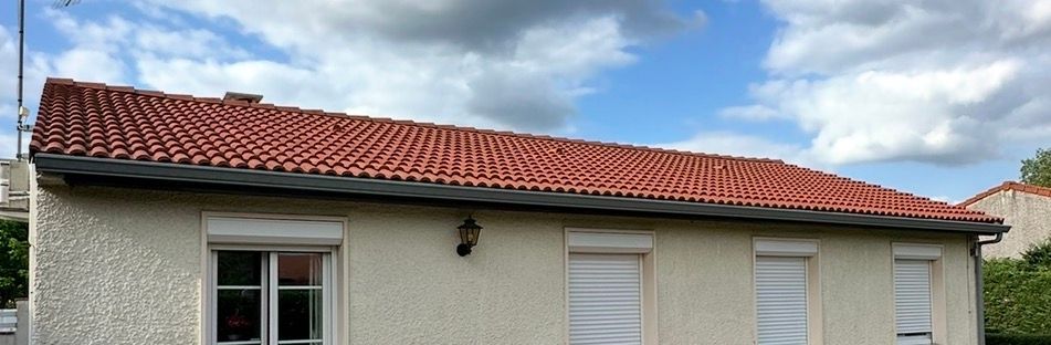 Un bâtiment d'un étage avec un toit de tuiles rouges et des murs clairs, sous un ciel nuageux.