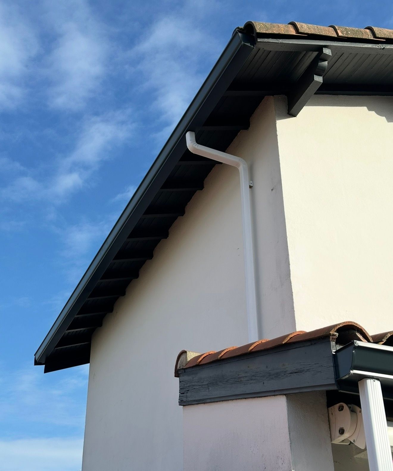 Maison blanche avec des boiseries sombres et une descente de gouttière blanche se détachant sur un ciel bleu.