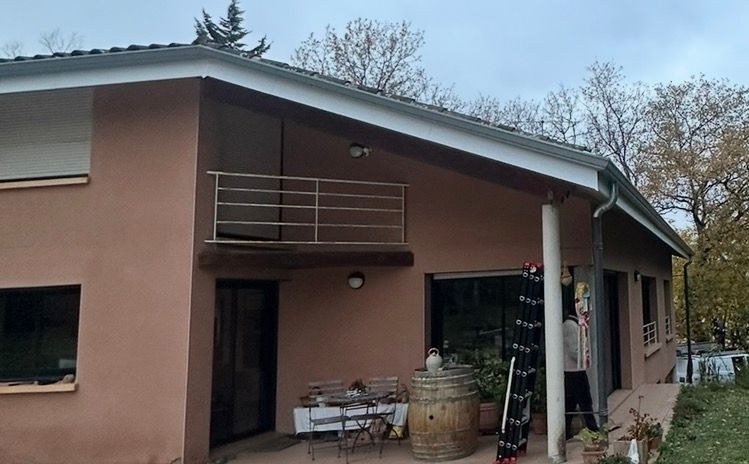 Maison à deux étages avec balcon et balustrade en métal, peinte en pêche. Arbres d'automne en arrière-plan.