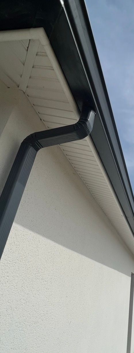 Gouttière noire en bordure d'un bâtiment blanc aux avant-toits visibles.