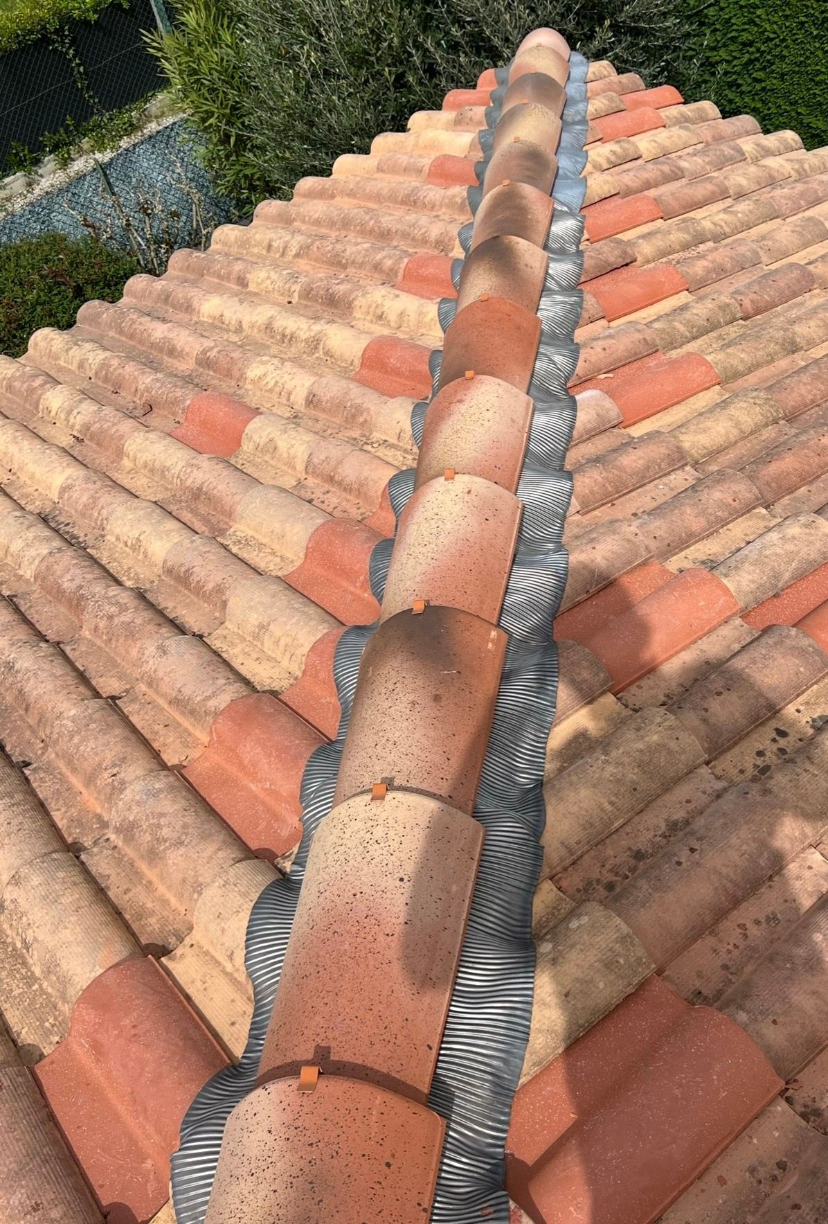 Toiture en tuiles de terre cuite avec solin gris au faîtage, vue de dessus.