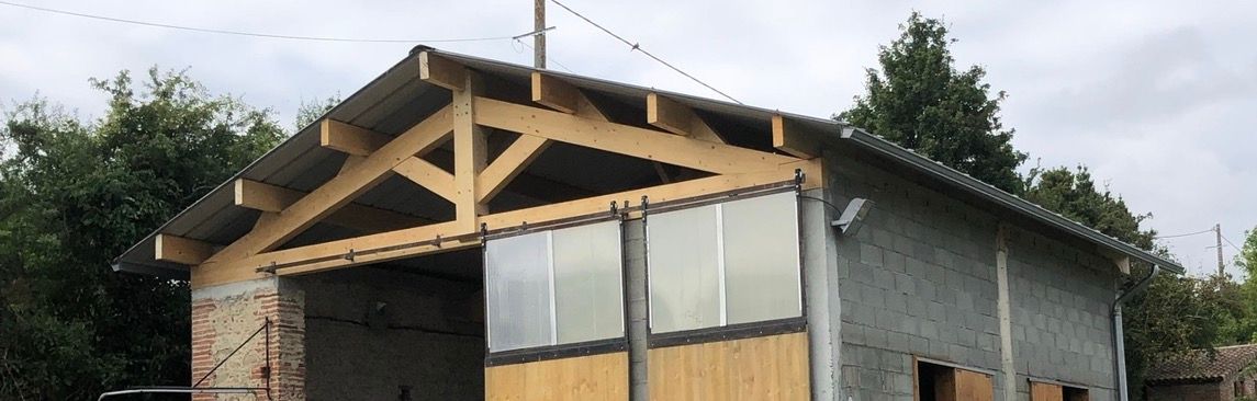 Un bâtiment avec une charpente en bois. Les murs du bâtiment sont en pierre et en parpaings.