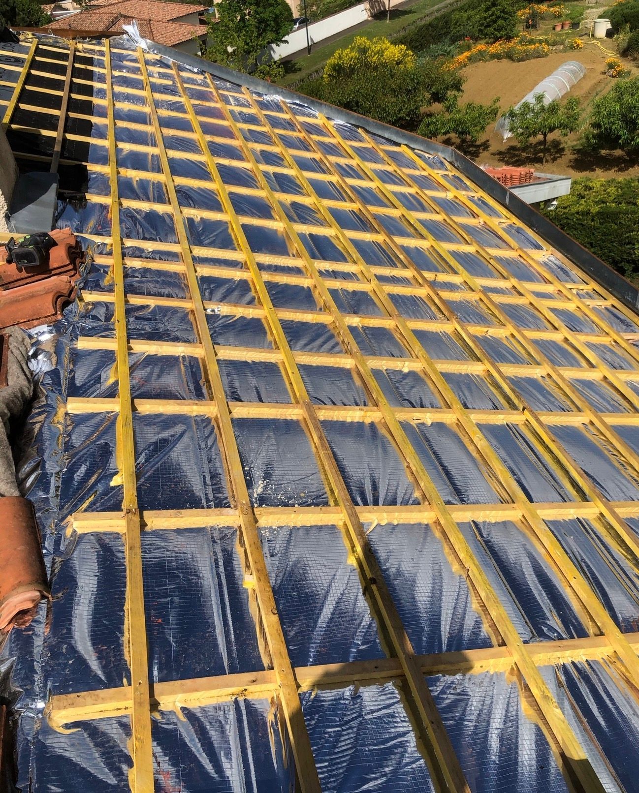 Toiture en construction ; poutres en bois posées sur un matériau sombre et réfléchissant.