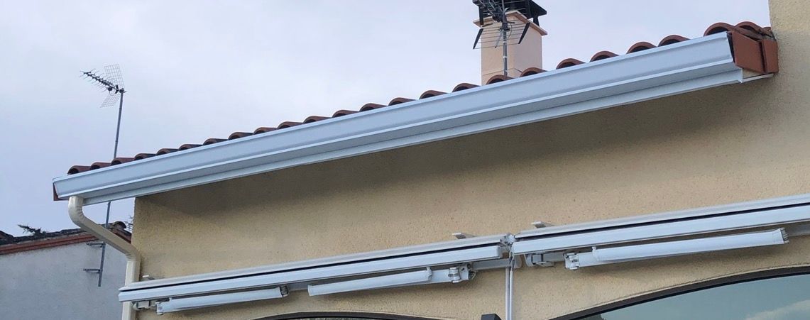 Bâtiment beige avec un auvent blanc sous un ciel nuageux.