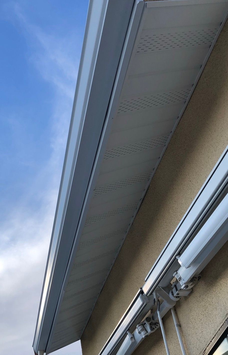 Sous-face et gouttière blanches sur une maison beige se détachant sur un ciel bleu.