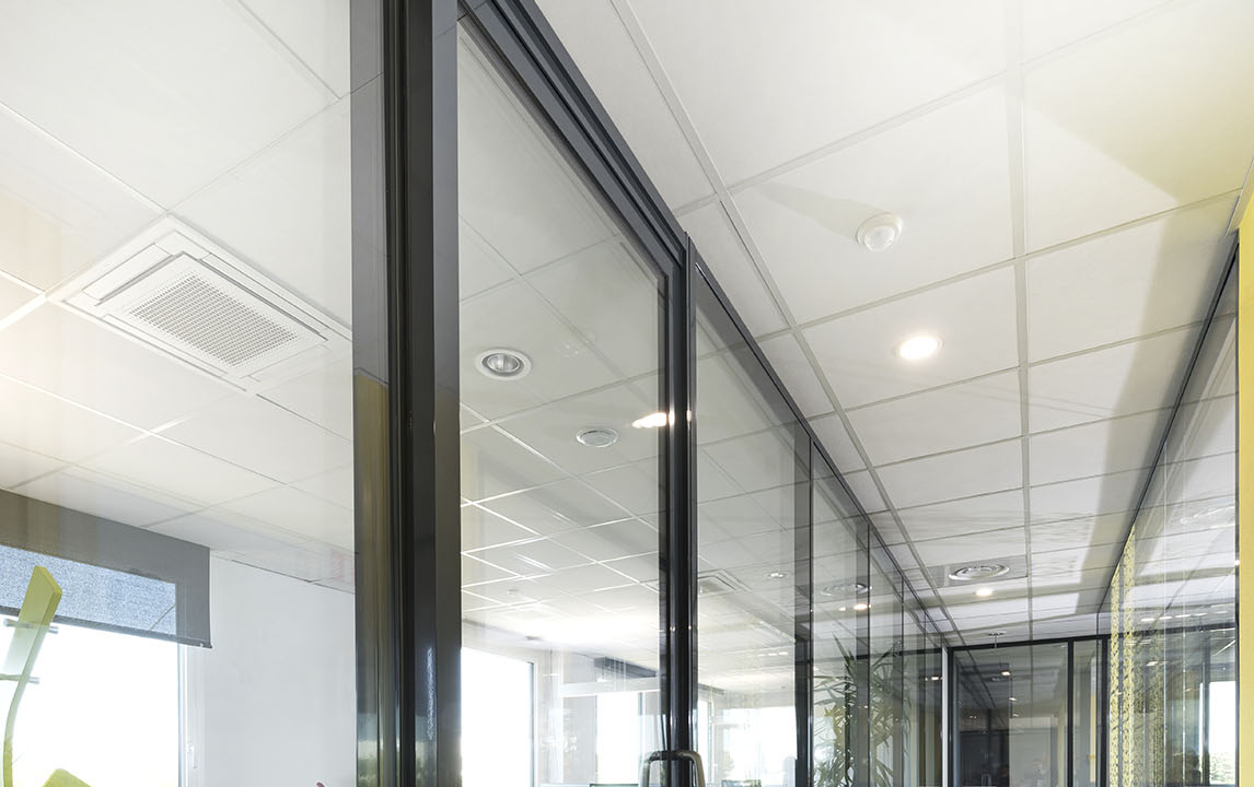 Espace de bureau intérieur avec murs en verre et plafond suspendu.