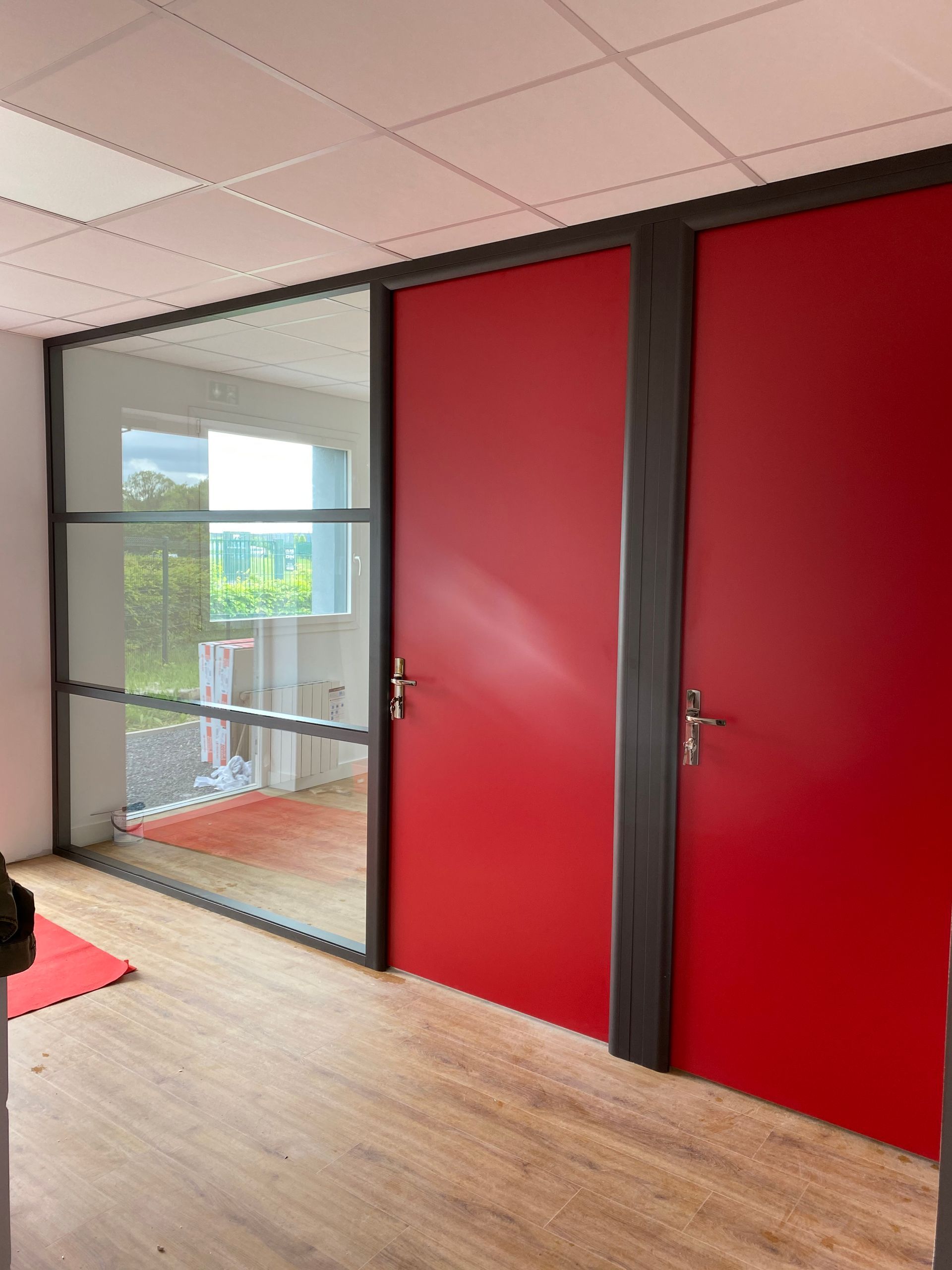 Portes rouges et paroi vitrée dans une pièce au parquet clair.