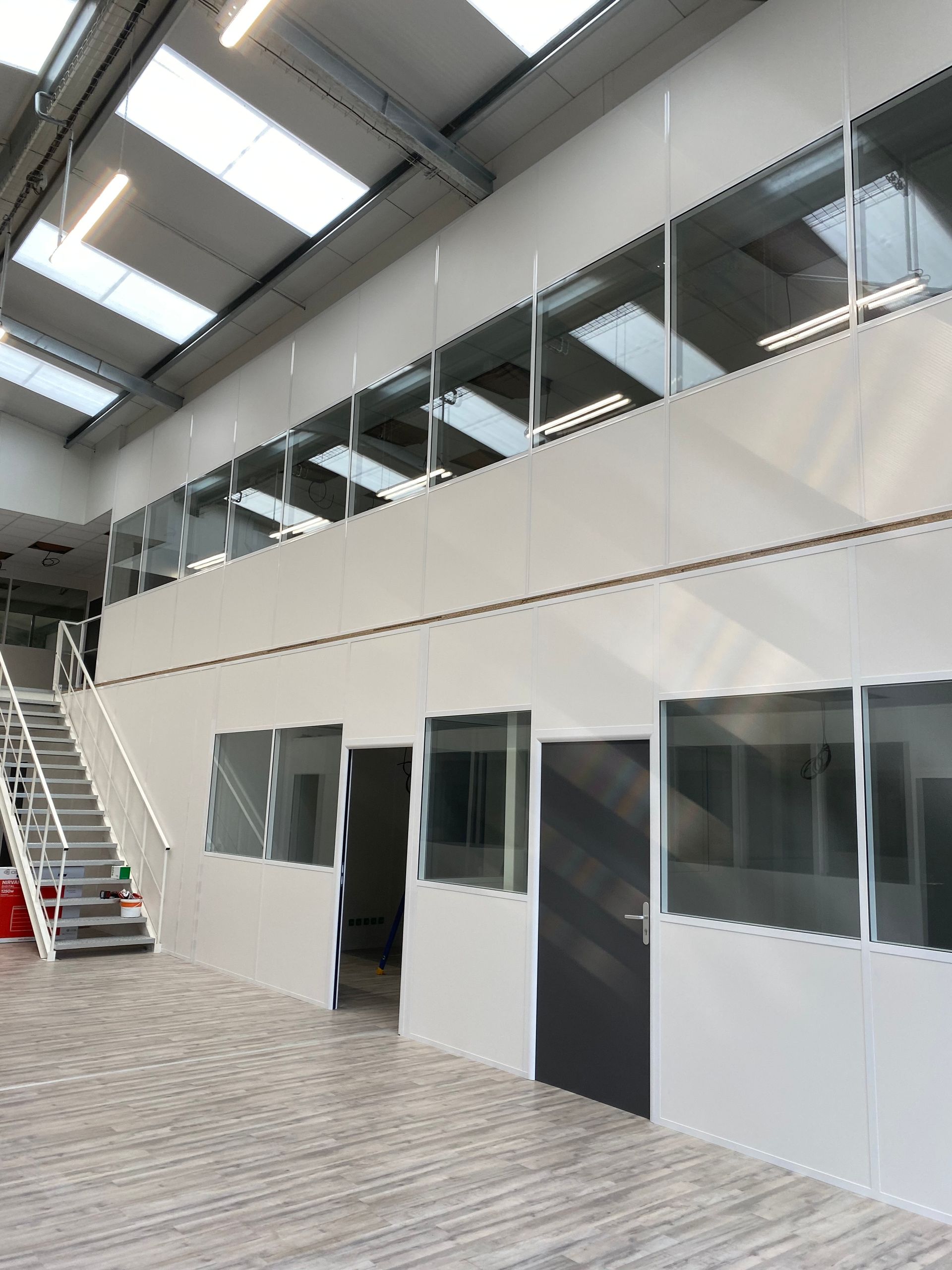 Intérieur industriel moderne et vide, avec murs blancs, puits de lumière, escalier et sol gris.