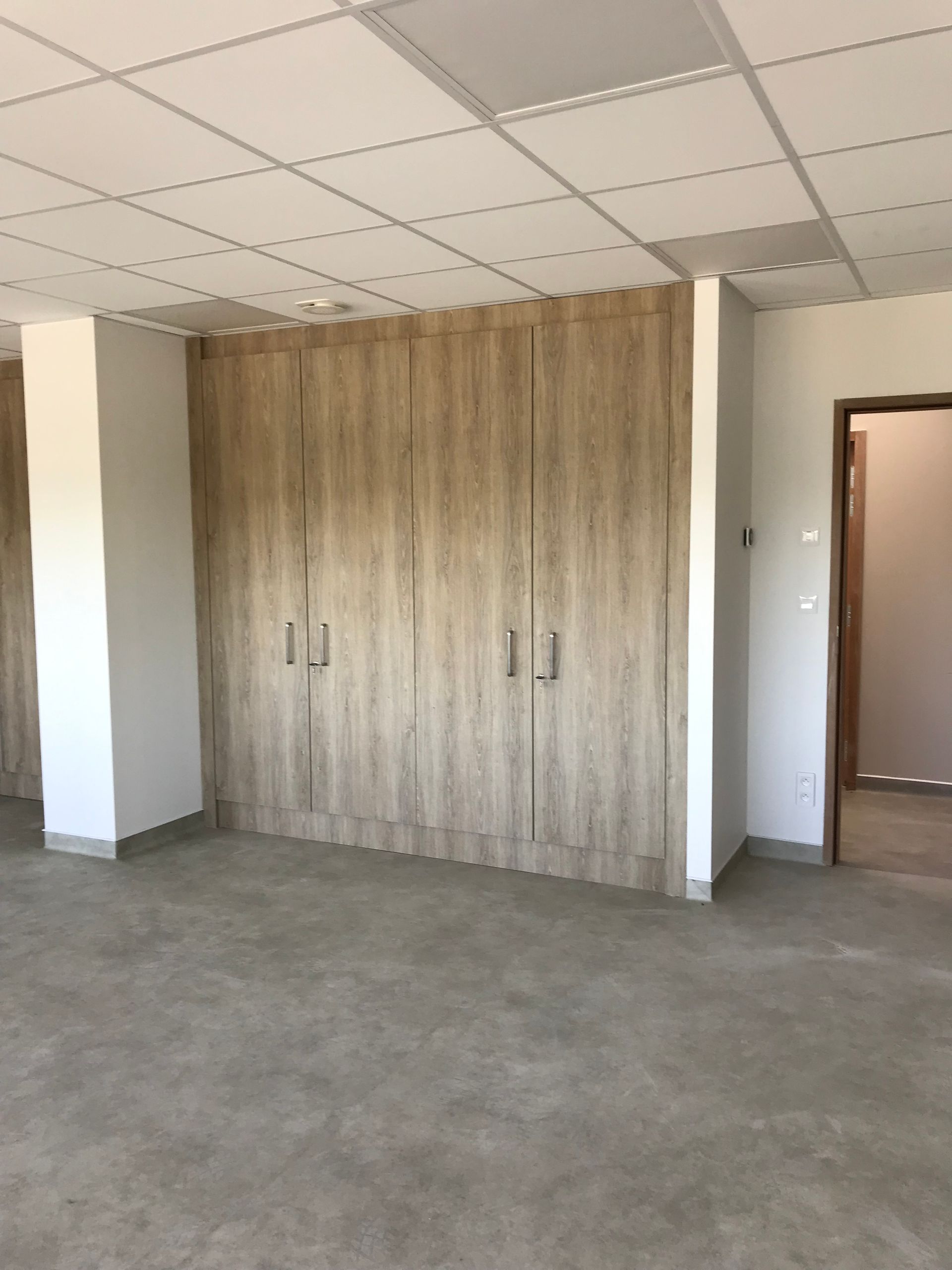 Pièce vide avec des placards en bois le long d'un mur. On aperçoit une porte et des colonnes blanches.