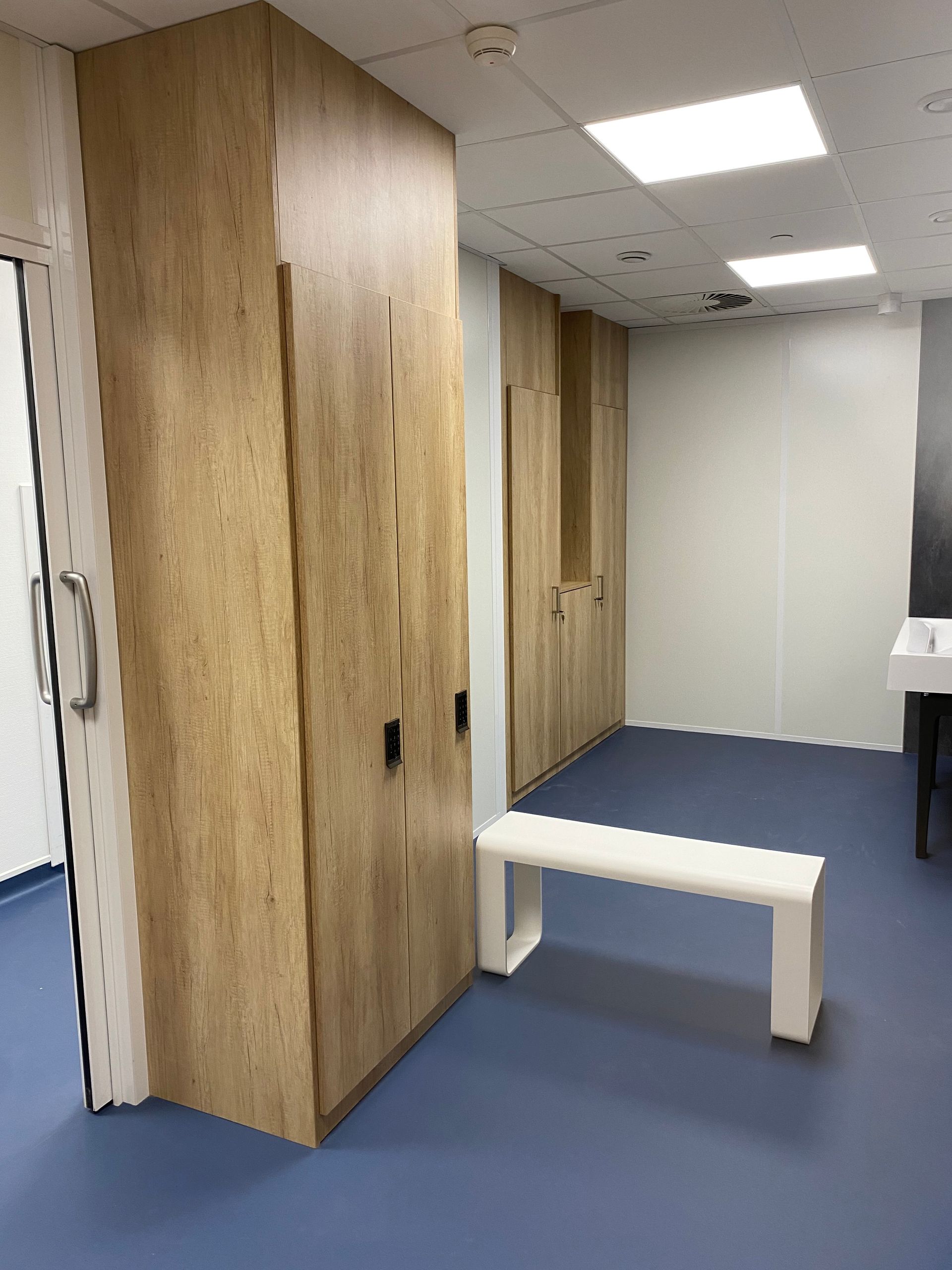 Des casiers en bois et un banc blanc dans une pièce au sol bleu et aux murs blancs.