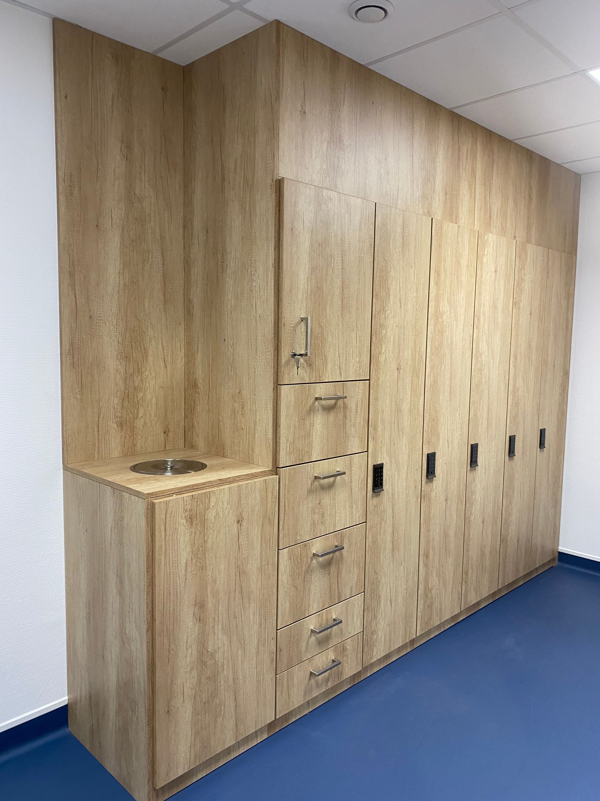 Meuble en bois intégré avec évier, tiroirs et étagère haute dans une pièce au sol bleu.