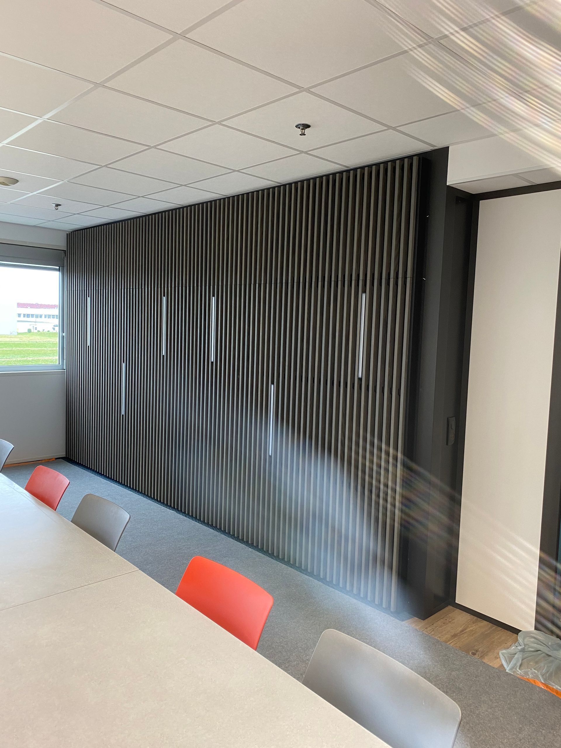 Salle de réunion avec une grande table et un panneau mural texturé abstrait. Les chaises sont orange et grises.