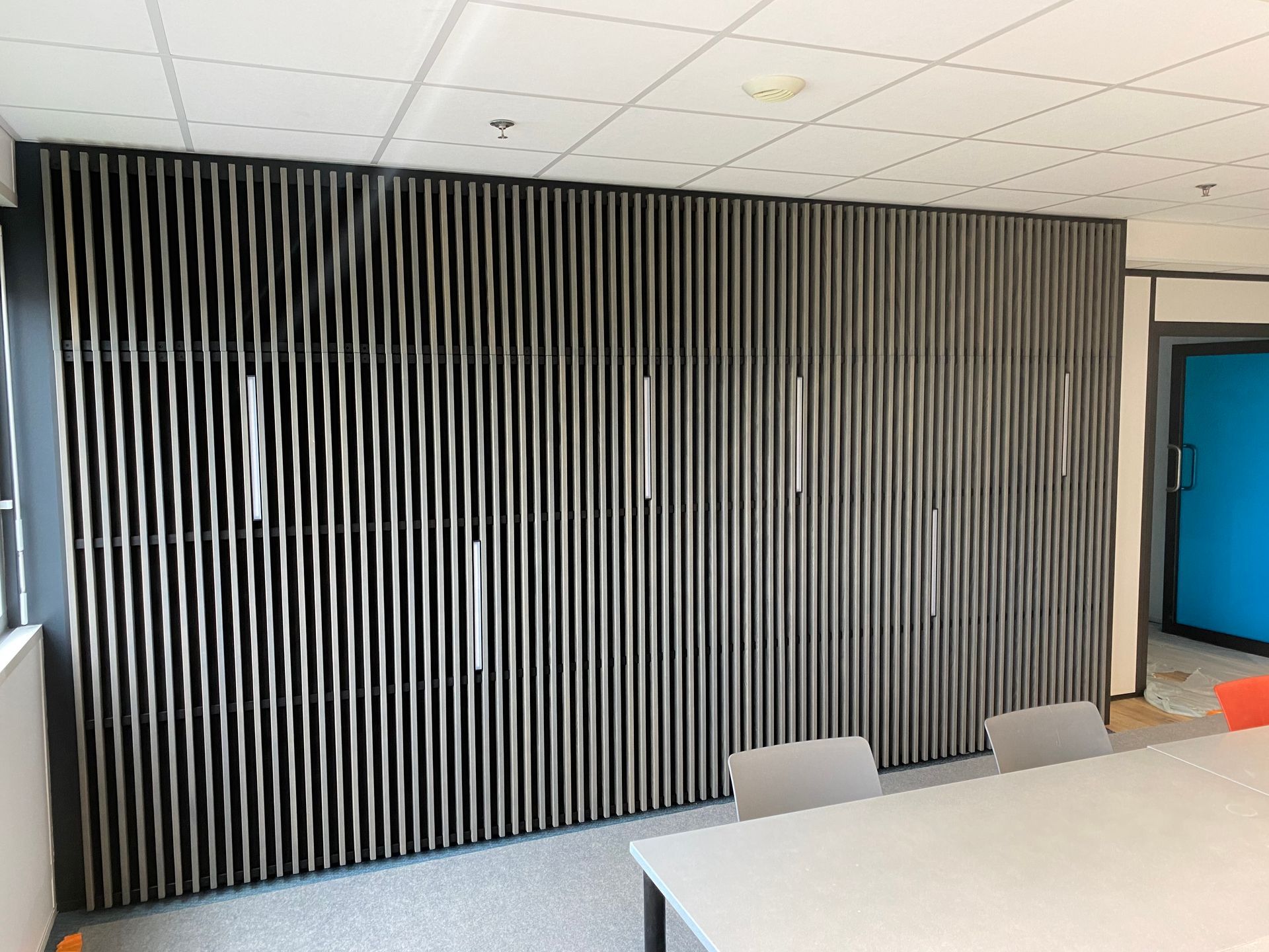 Mur à claire-voie avec éclairage vertical intégré, plafond blanc et table devant.