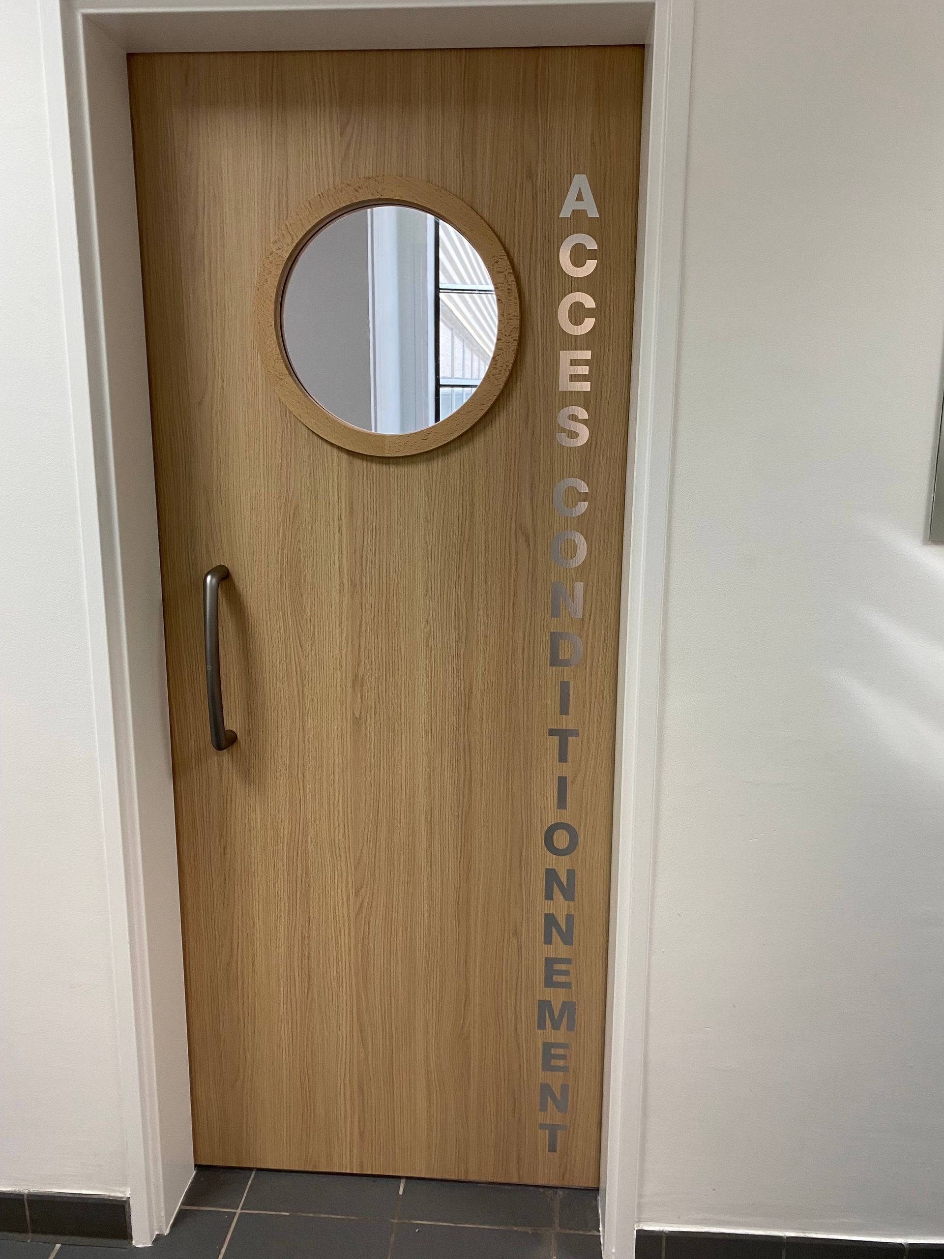 Porte en bois avec fenêtre ronde ; texte « ACCÈS CONDITIONNEMENT » en vertical.