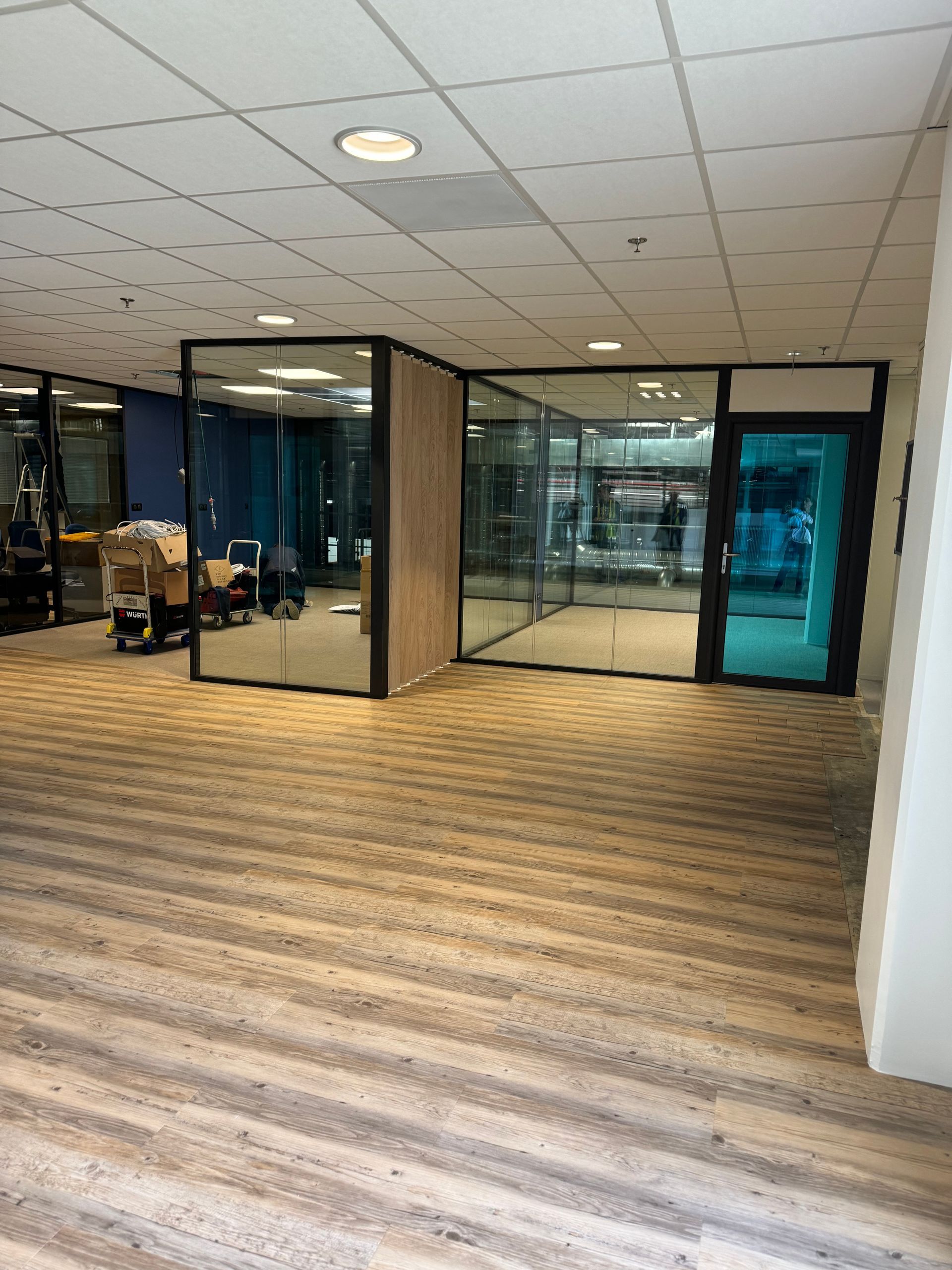 Intérieur de bureau avec des pièces aux parois vitrées, moquette beige et porte turquoise.
