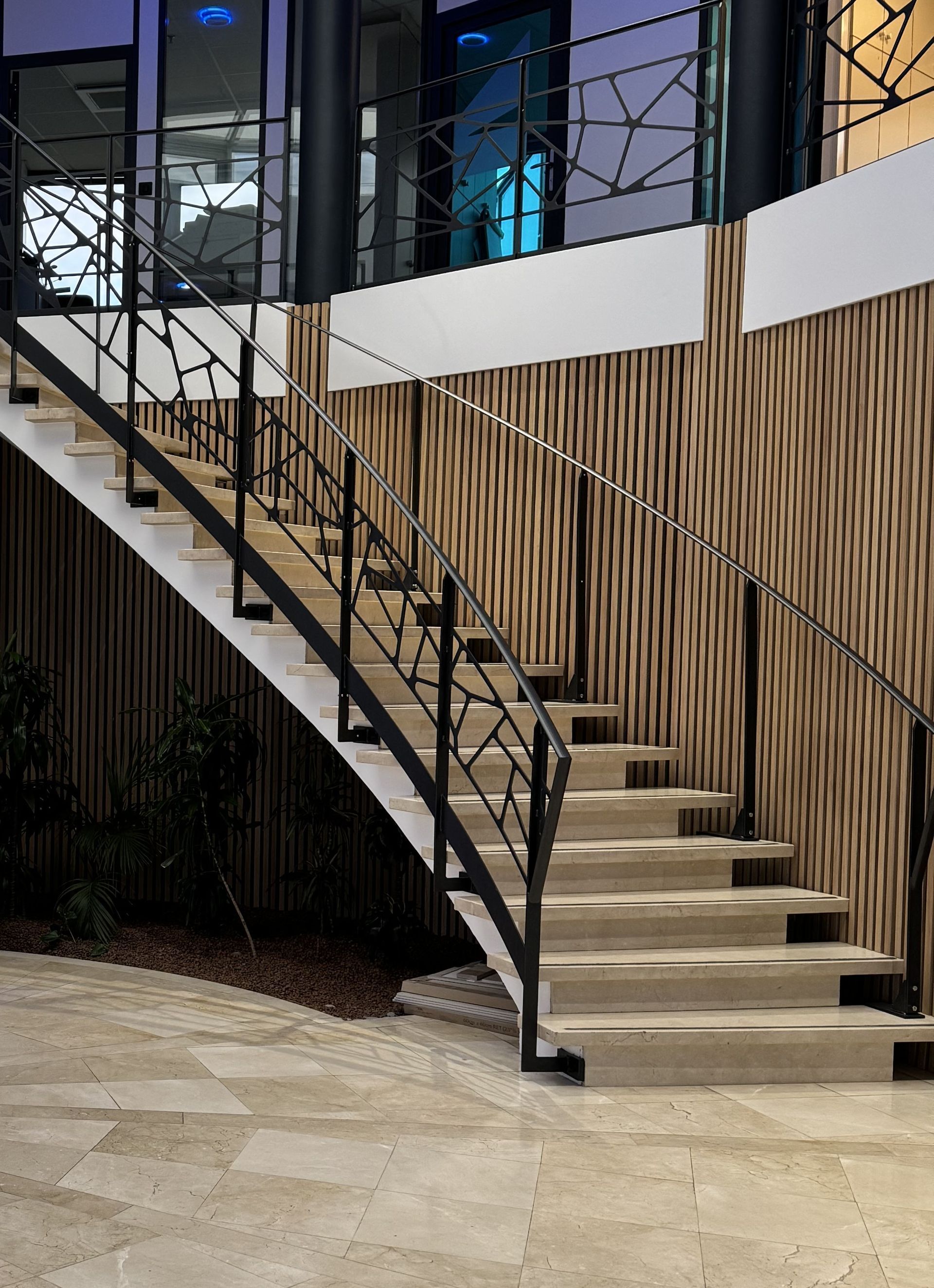 Escalier avec marches en pierre claire, rampe en fer noir et lambris mural.