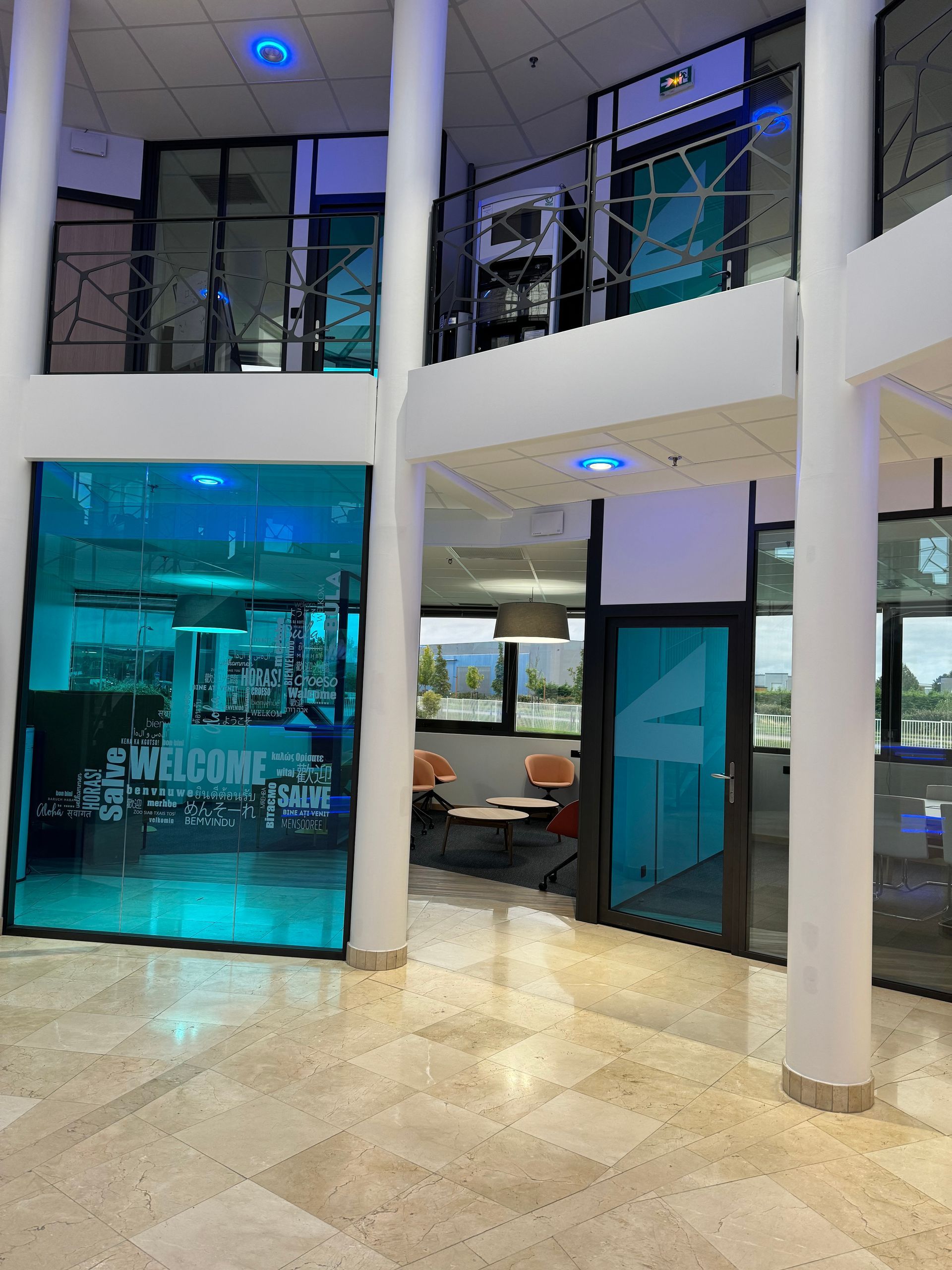 Intérieur d'un bâtiment moderne avec des touches turquoise et des murs de verre. Texte de bienvenue visible.