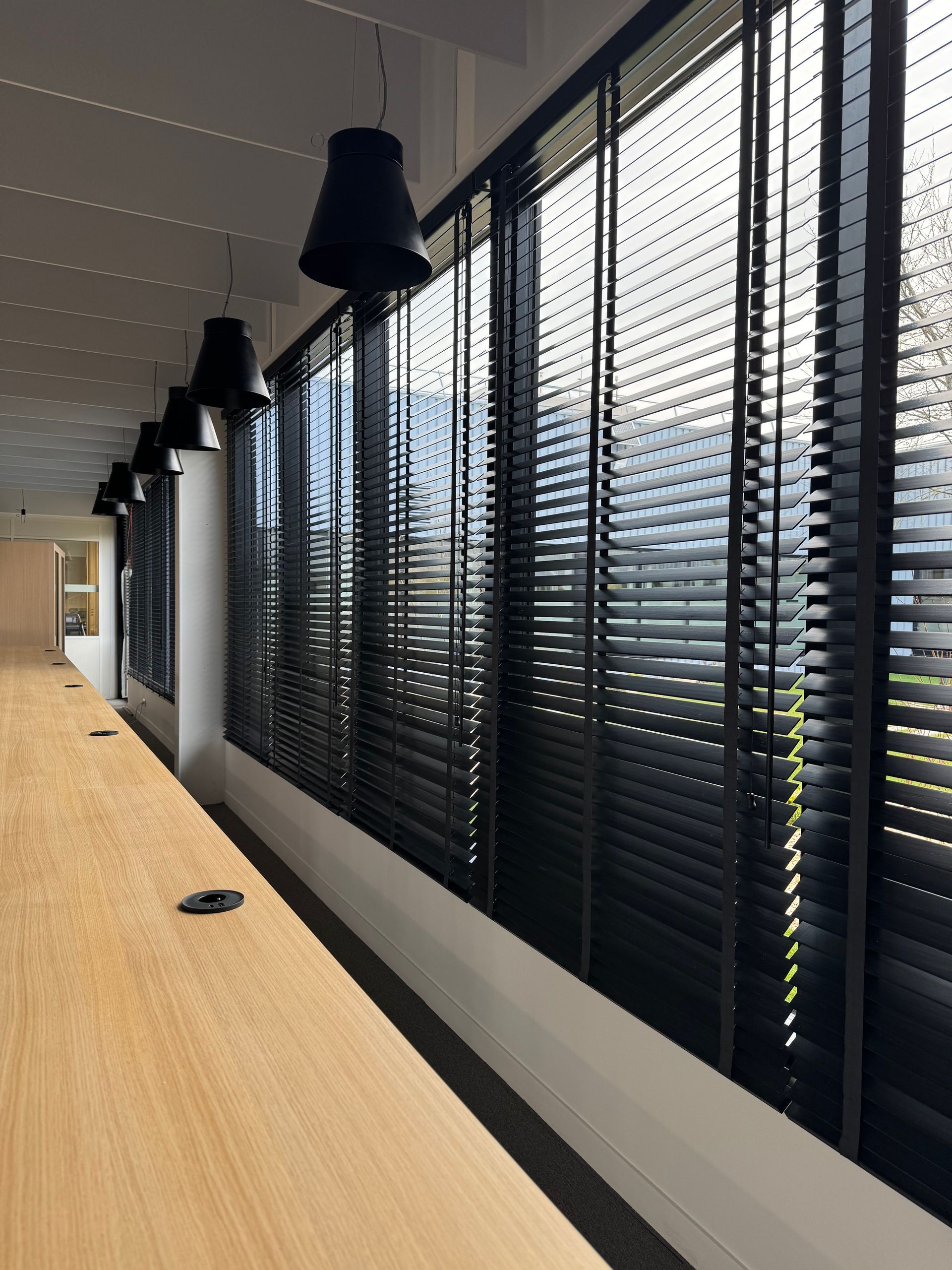 Long comptoir en bois avec lampes noires et stores.