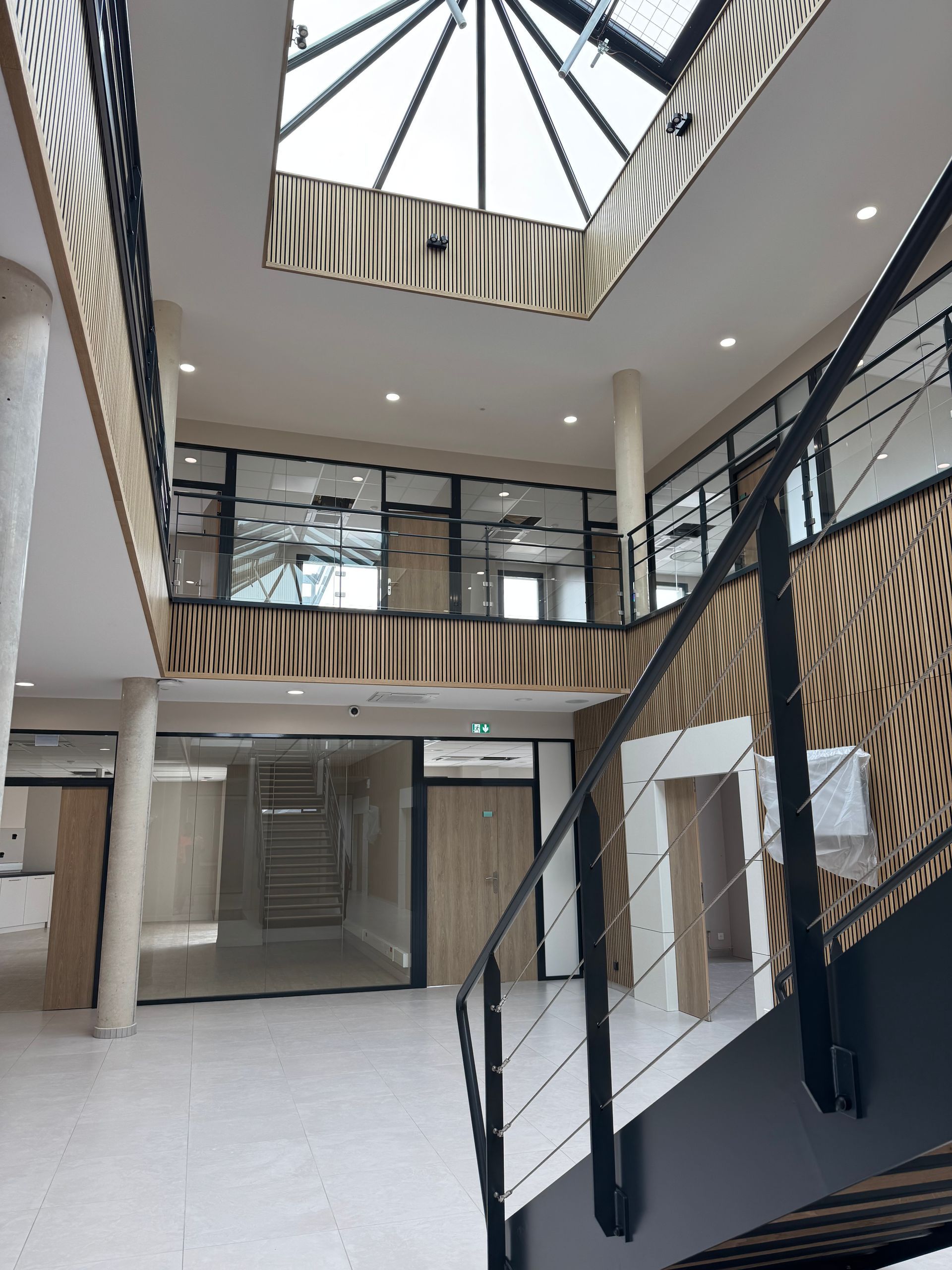 Vue intérieure d'un bâtiment moderne avec escalier, parois vitrées et puits de lumière.