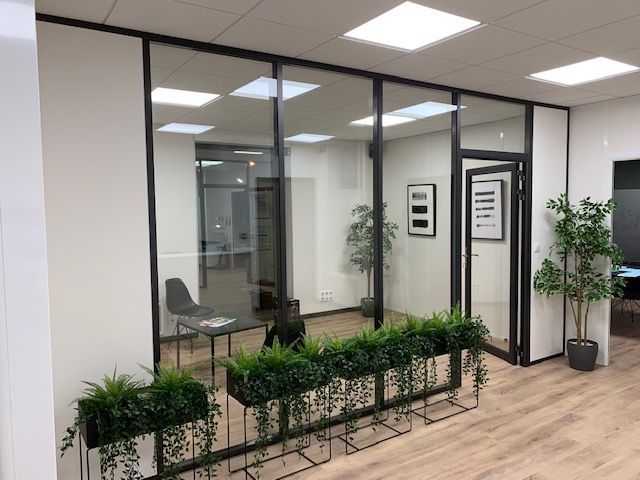 Intérieur de bureau avec bureau aux parois vitrées, garnitures noires, plantes et parquet en bois clair.