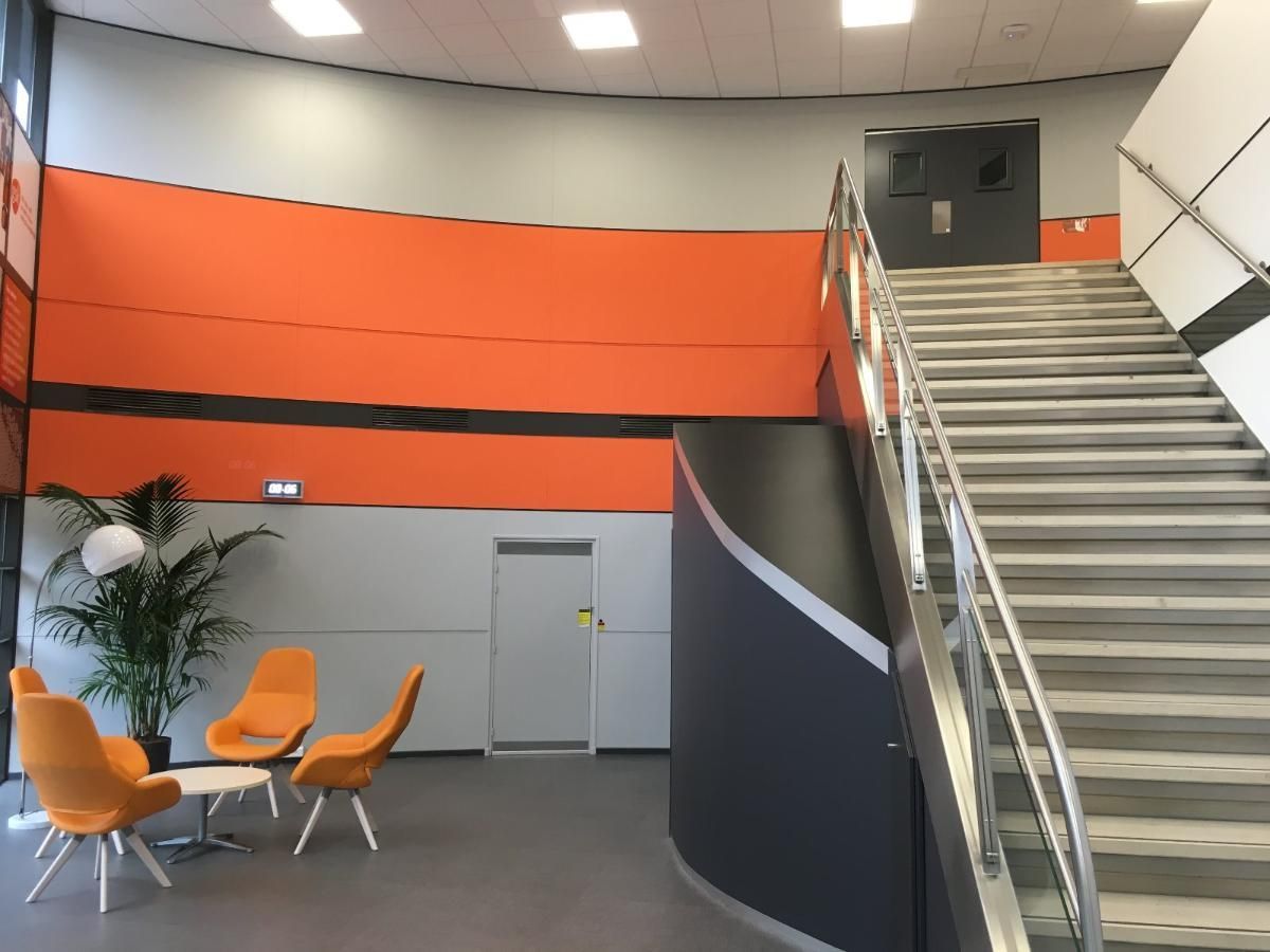 Intérieur moderne avec mur orange, escalier, chaises et plante en pot.