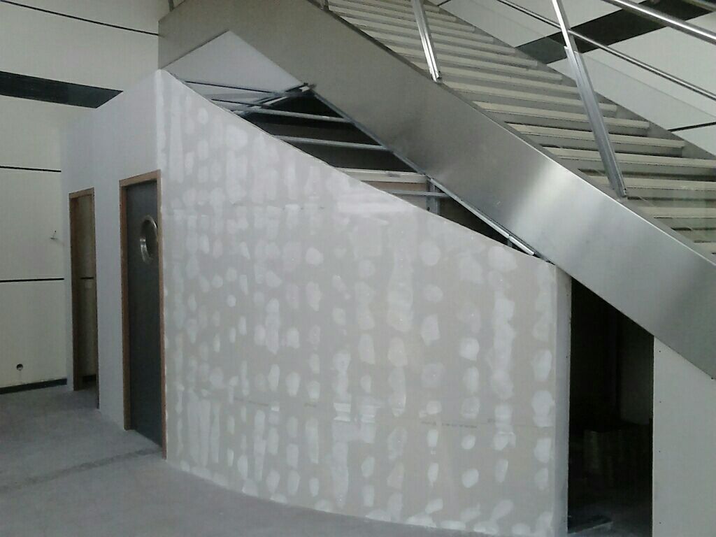 Espace intérieur avec escalier, mur incurvé en construction et porte.