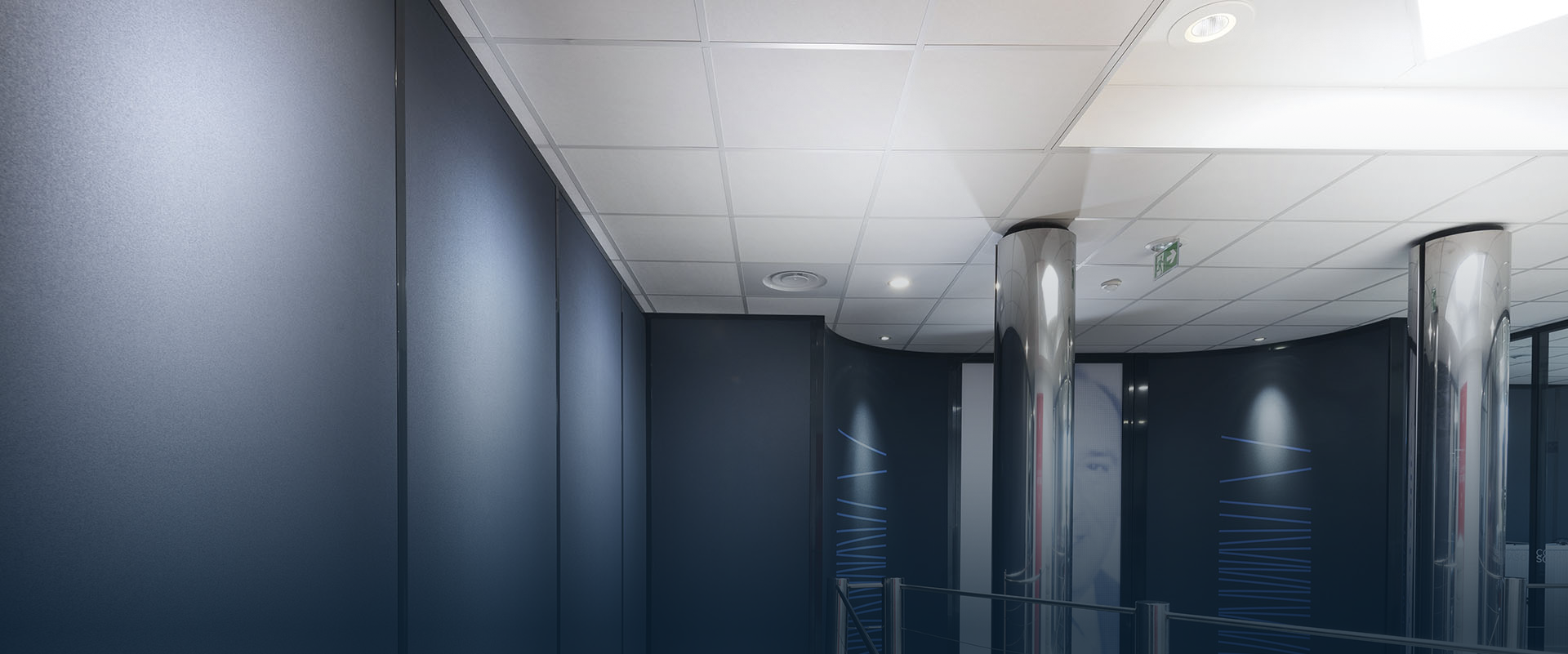 Un couloir moderne avec des murs bleu foncé, un plafond blanc et des piliers argentés.