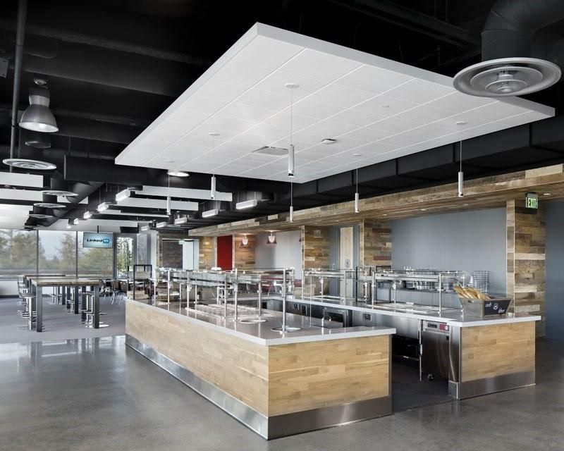 Cafétéria moderne avec comptoirs de buffet, tables et plafond suspendu avec éclairage encastré.