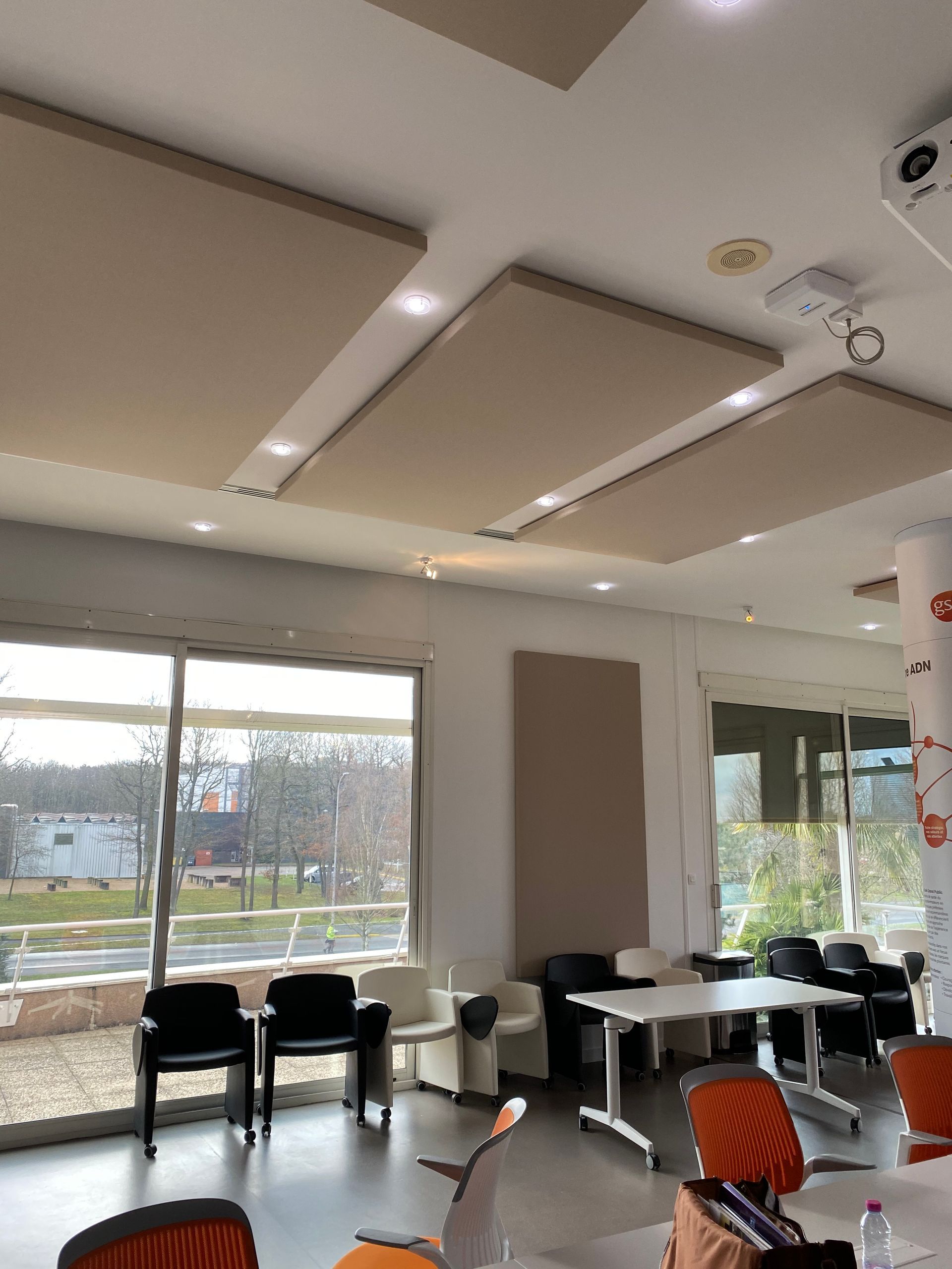 Salle de conférence avec de grandes fenêtres, panneaux d'insonorisation au plafond, chaises et tables.