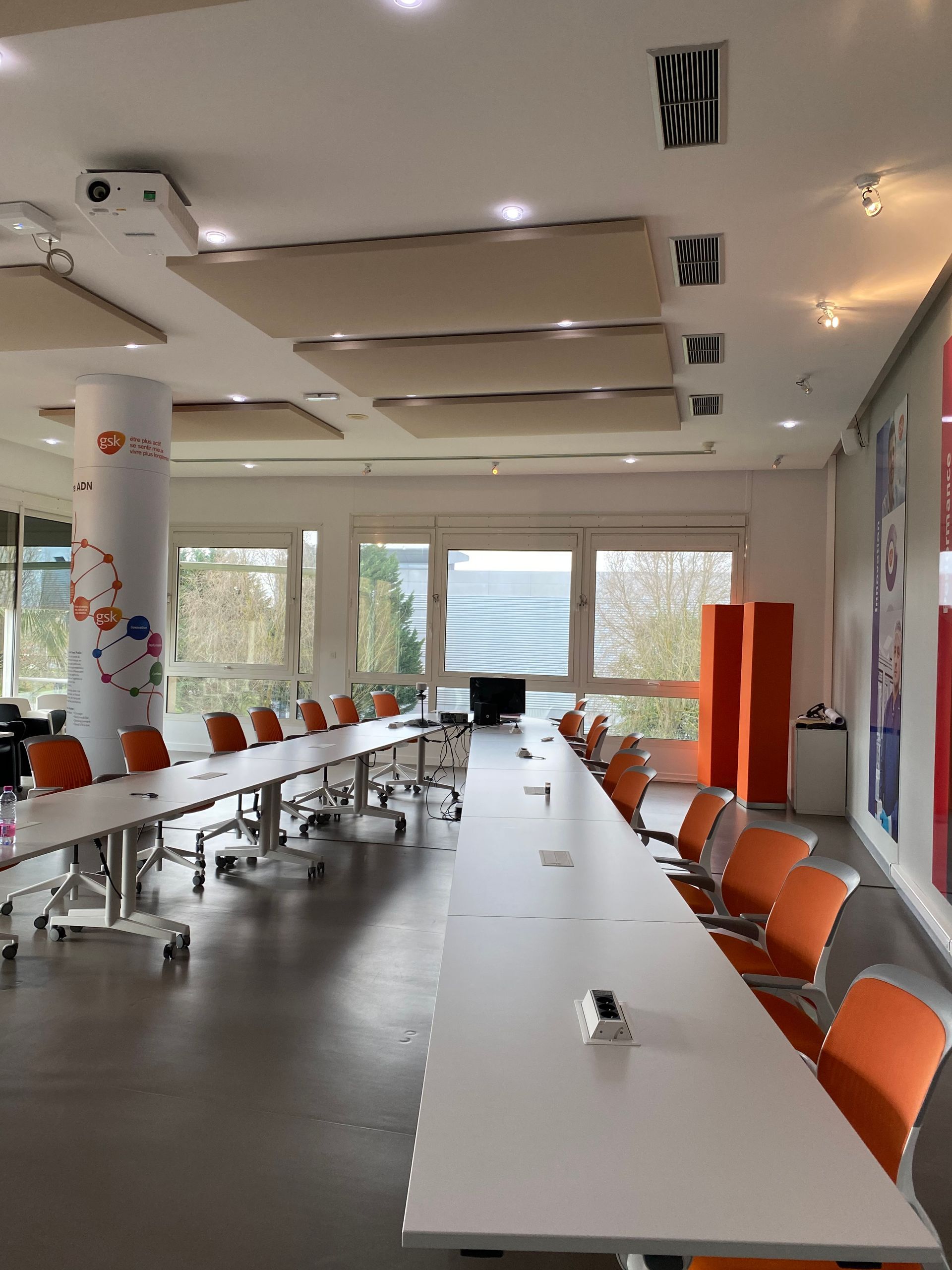 Longue table de conférence avec chaises orange, fenêtres et insonorisation dans une pièce moderne.