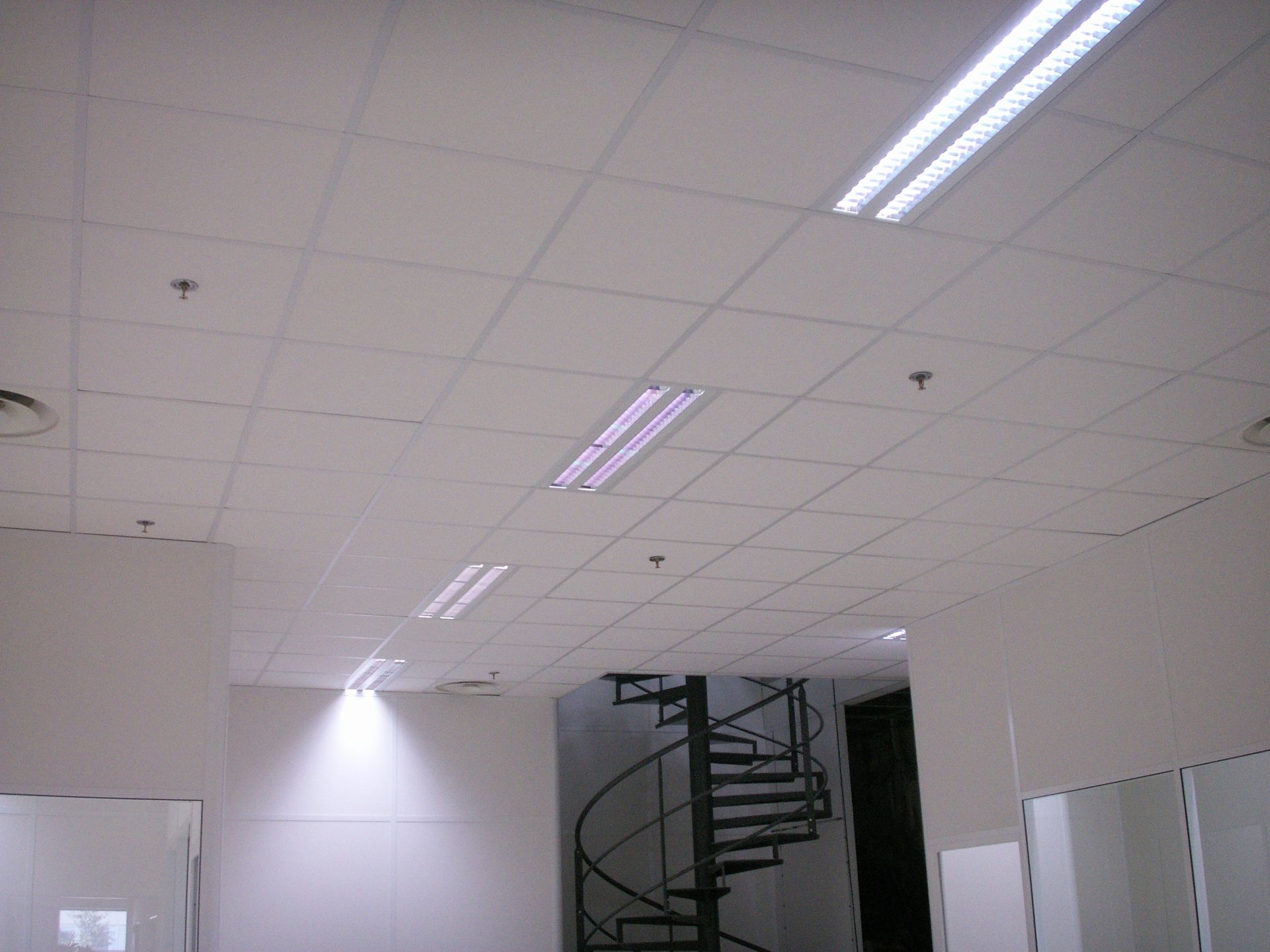 Plafond blanc de bureau avec éclairage encastré et escalier en colimaçon.