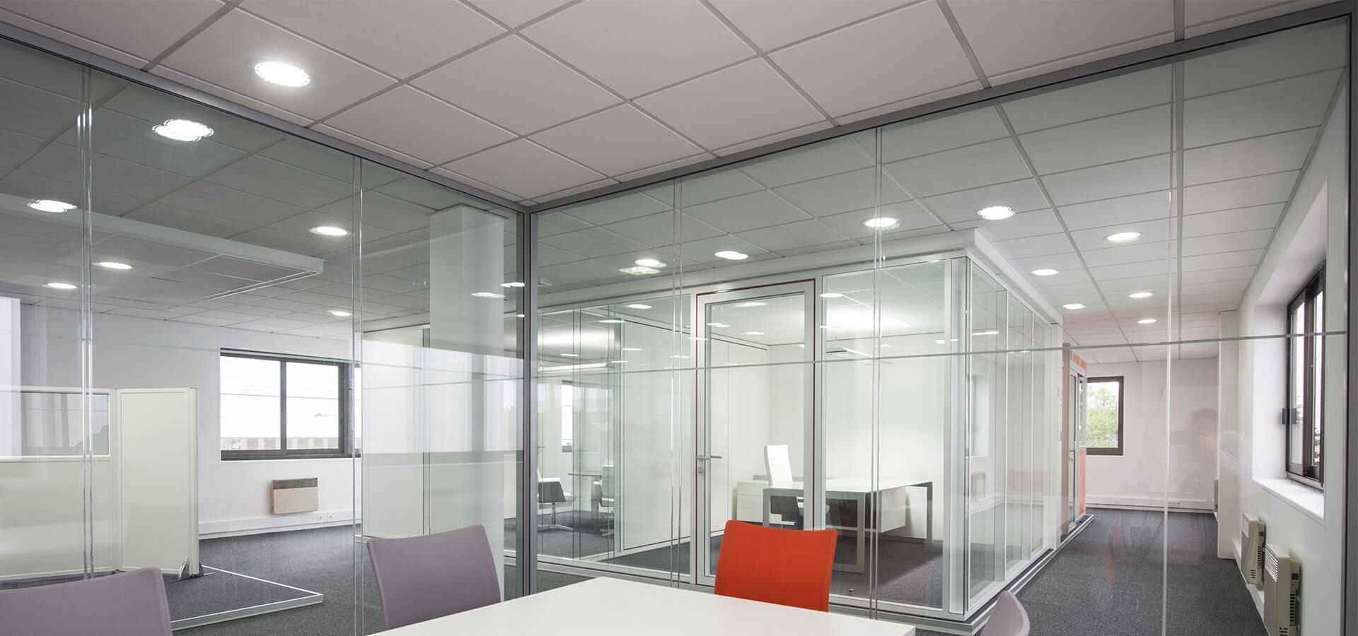 Intérieur de bureau moderne avec salles vitrées et table de conférence. Tons blancs et gris, éclairage encastré.