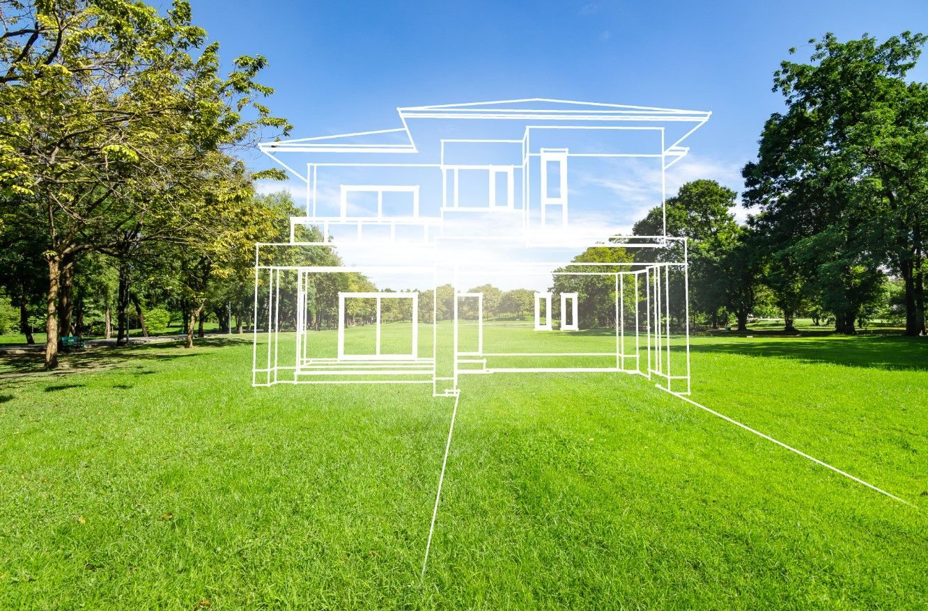 White wireframe house outline on a bright green lawn in a sunny park with trees.