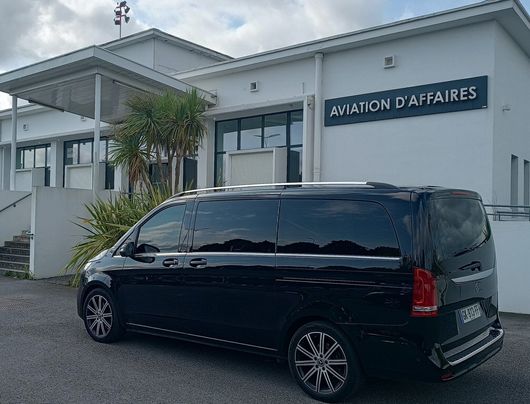 Un SUV noir est garé devant un bâtiment blanc portant l'inscription Aviation d'Affaires.