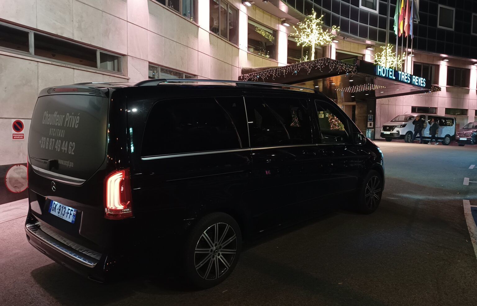 Une Mercedes noire garée le long d'un trottoir éclairé devant un bâtiment, la nuit.