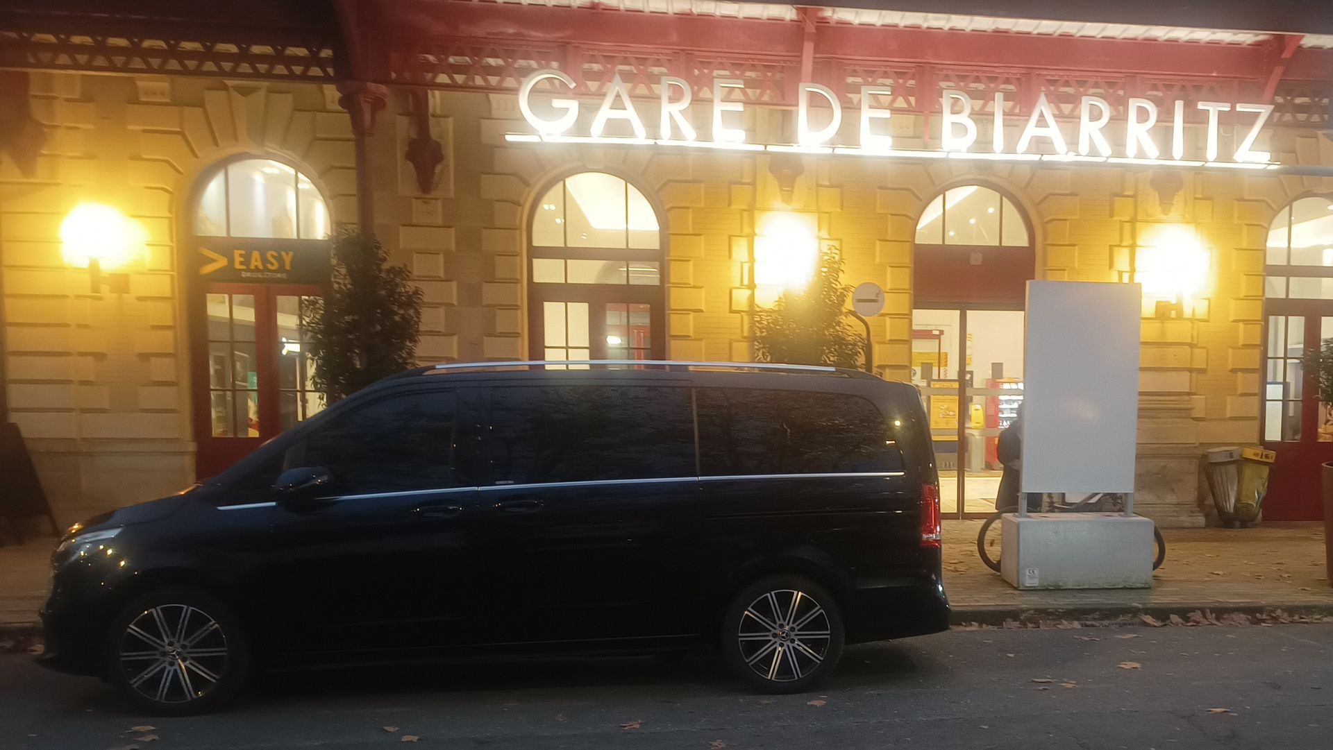 Une Mercedes noire est garée dans une rue, devant un bâtiment en briques et des panneaux de signalisation.