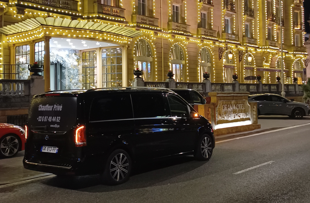 Une Mercedes noire garée devant l'entrée illuminée d'un hôtel de luxe, la nuit.