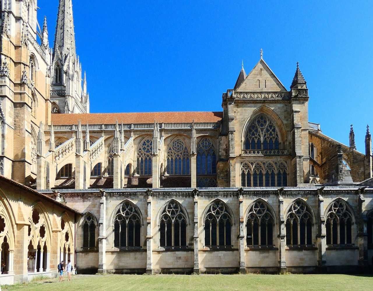 Cloître de cathédrale gothique avec ses arches de pierre, ses hautes fenêtres et un ciel bleu surplombant une cour verdoyante