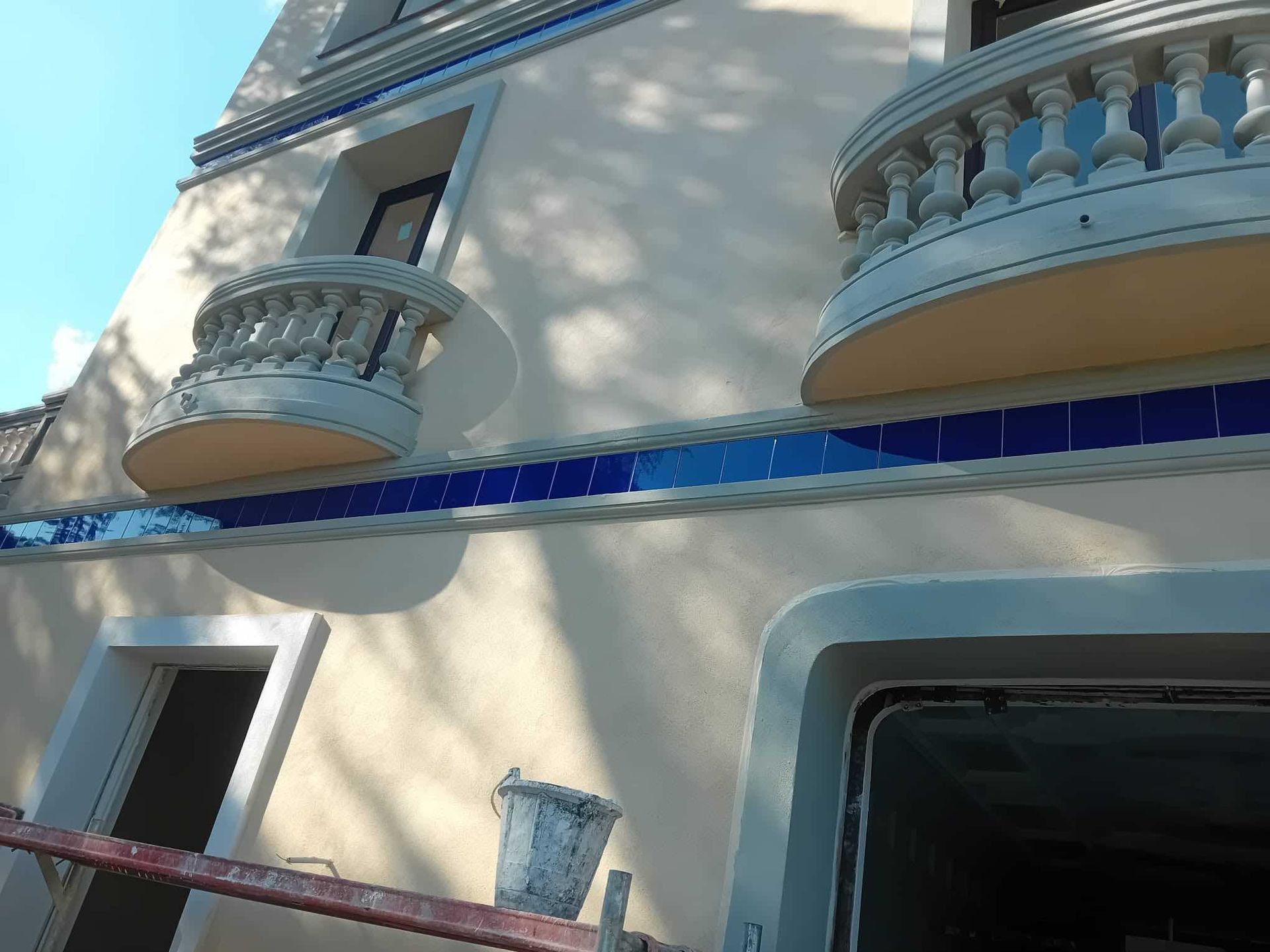Edificio beige con detalles de azulejos azules y balcones ornamentados bajo un cielo azul.