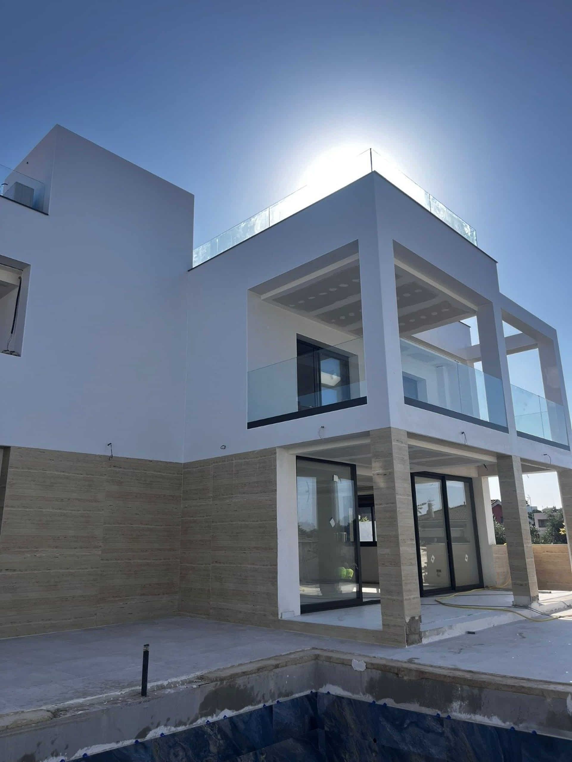 Moderna casa blanca con balcones de cristal y base de piedra beige bajo un sol brillante.