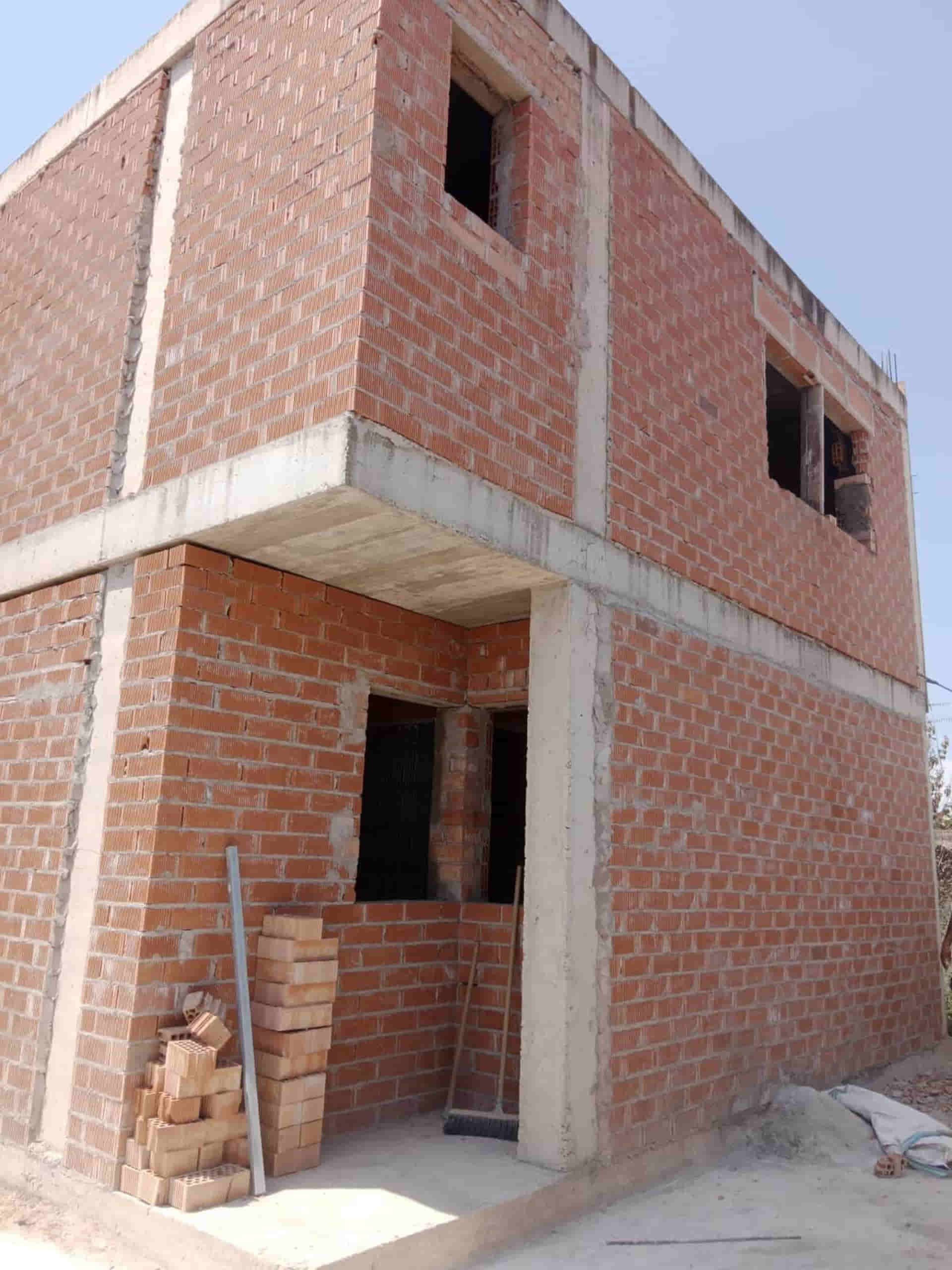 Edificio de ladrillo de dos pisos en construcción con vigas de hormigón a la vista y aberturas de ventanas.