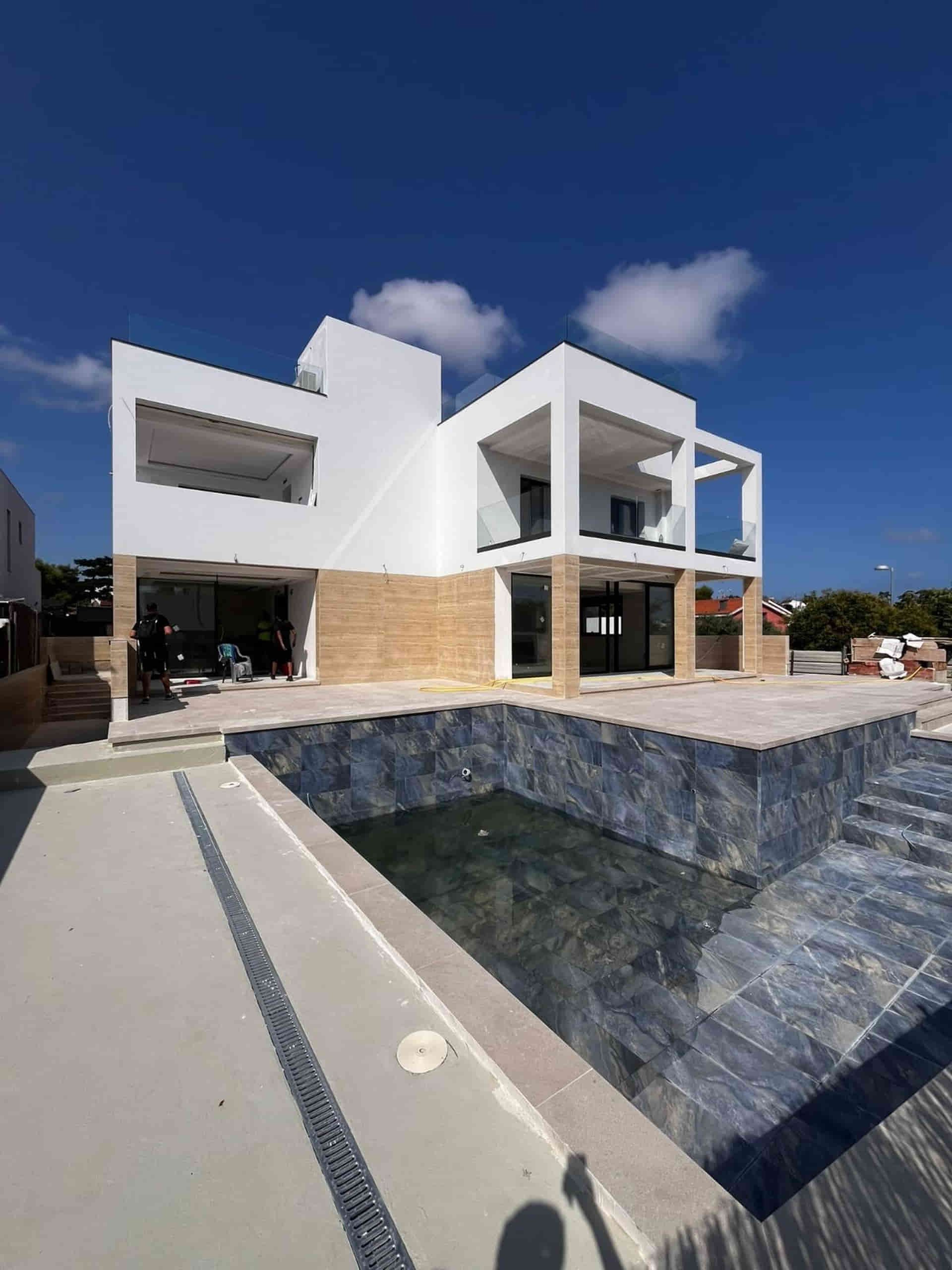 Moderna casa blanca con piscina, cielo azul claro.