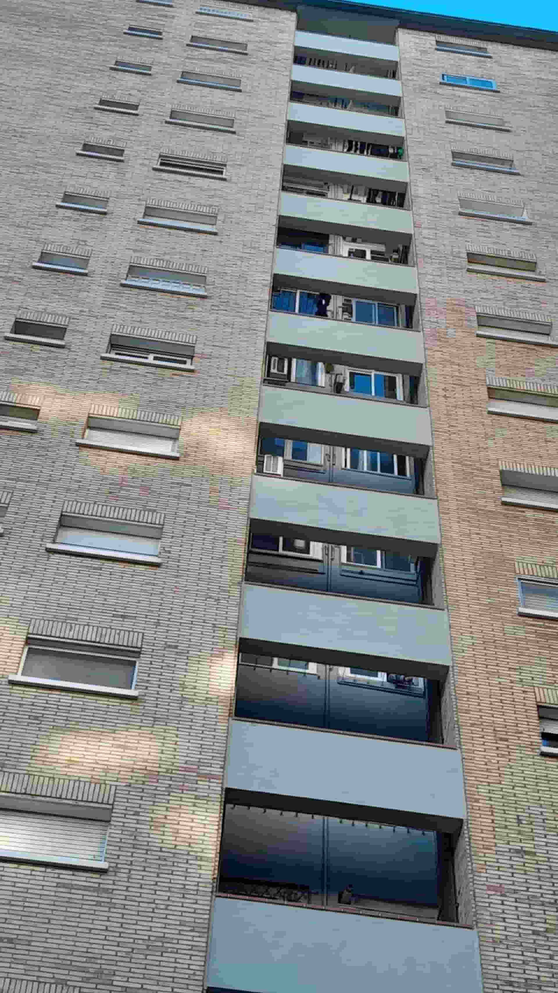 Edificio alto de apartamentos de ladrillo con muchas ventanas y balcones, visto desde abajo.